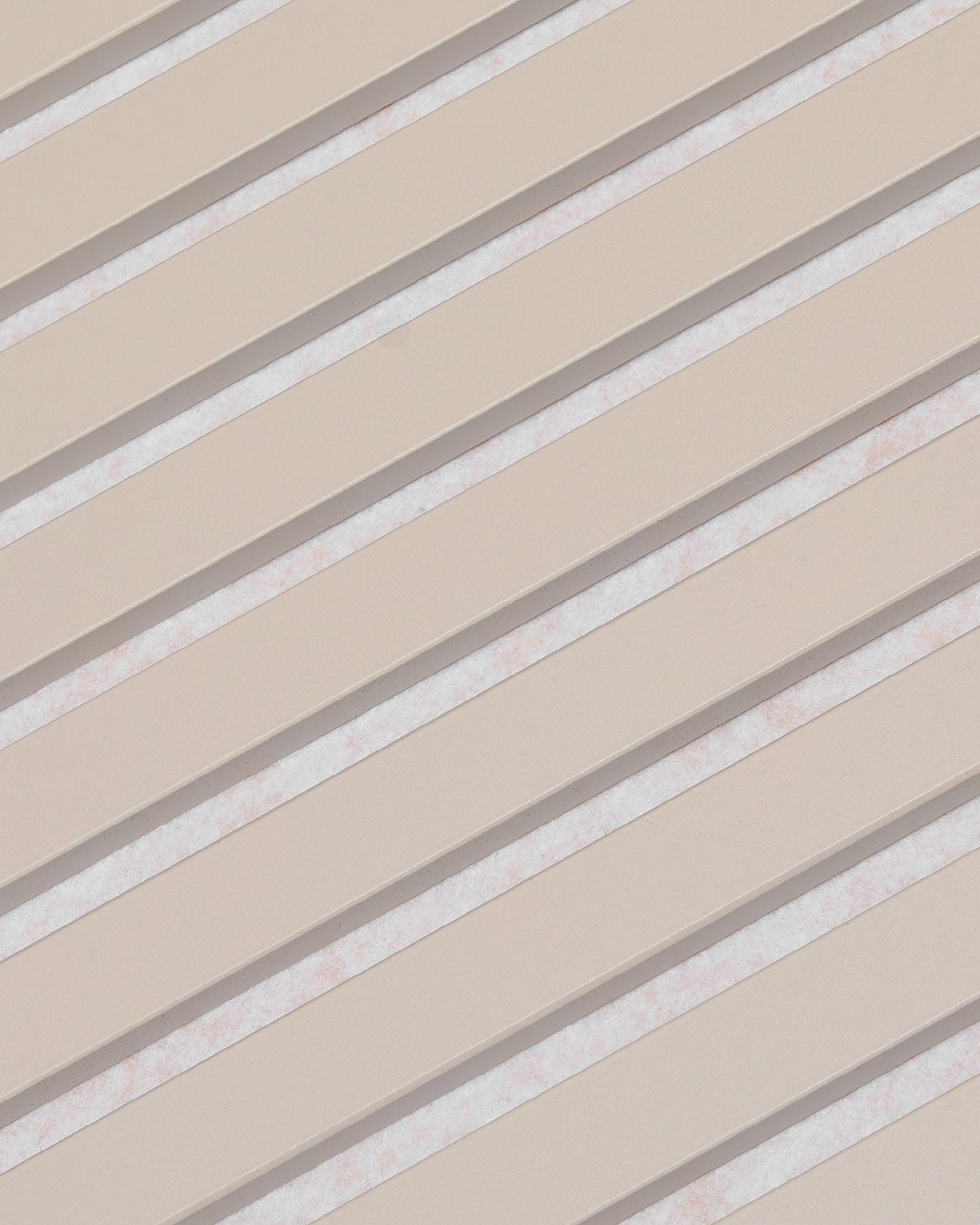 Le doghe diagonali beige con spazi bianchi formano un motivo a strisce sul pannello acustico WoodUpp Akupanel, con finitura in feltro Soft Linen Light Beige, 240x60 cm.