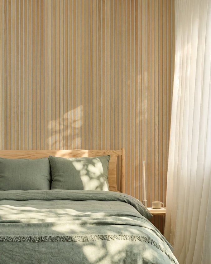 Camera da letto nordica minimalista con biancheria da letto verde salvia e una parete acustica a doghe WoodUpp Classic Rovere Akupanel; la luce del sole crea ombre morbide sul letto.