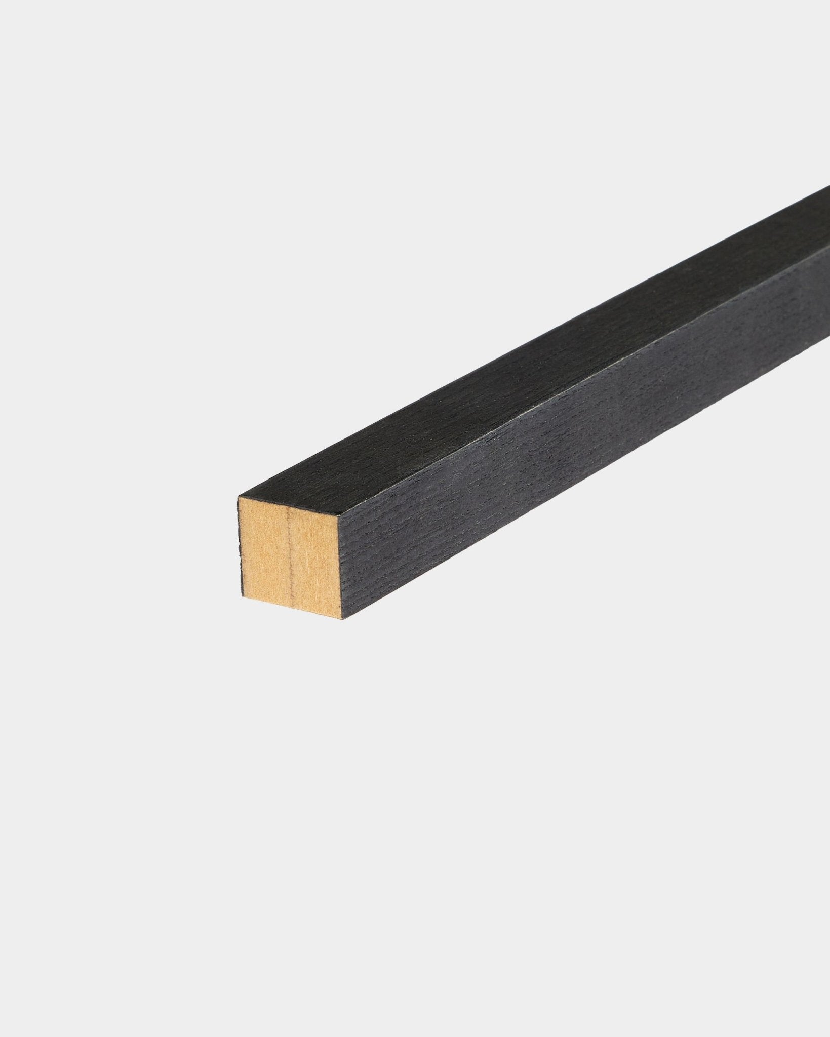WoodUpp Black Lamella terminale in frassino, 2,2 cm, pensata per l’installazione Akupanel Pannello acustico, appoggiata su una superficie bianca con un’estremità non rifinita.
