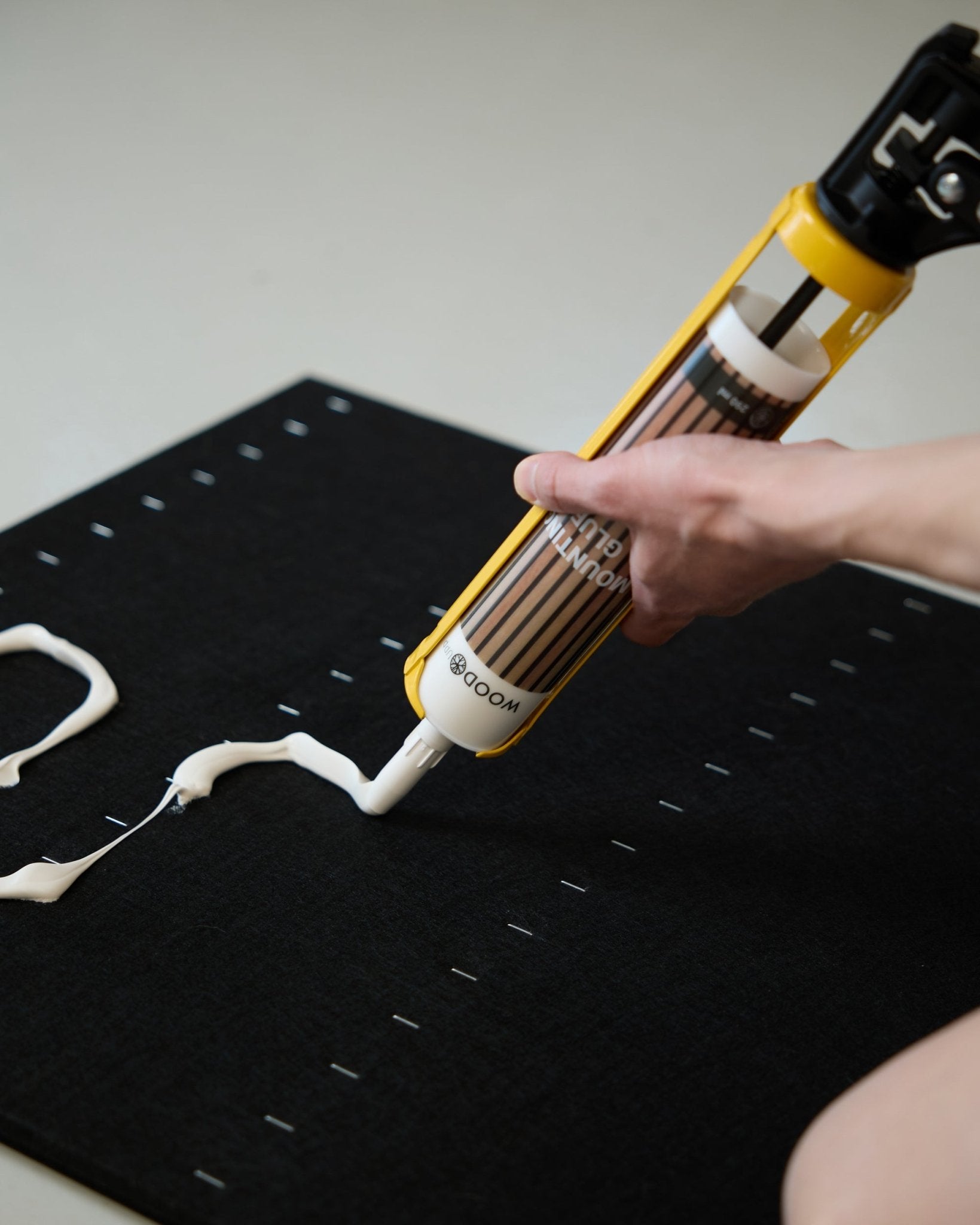 Una mano applica Colla bianco a zigzag con la WoodUpp Pistola per Colla (290 ml) su una superficie Pannello acustico black.
