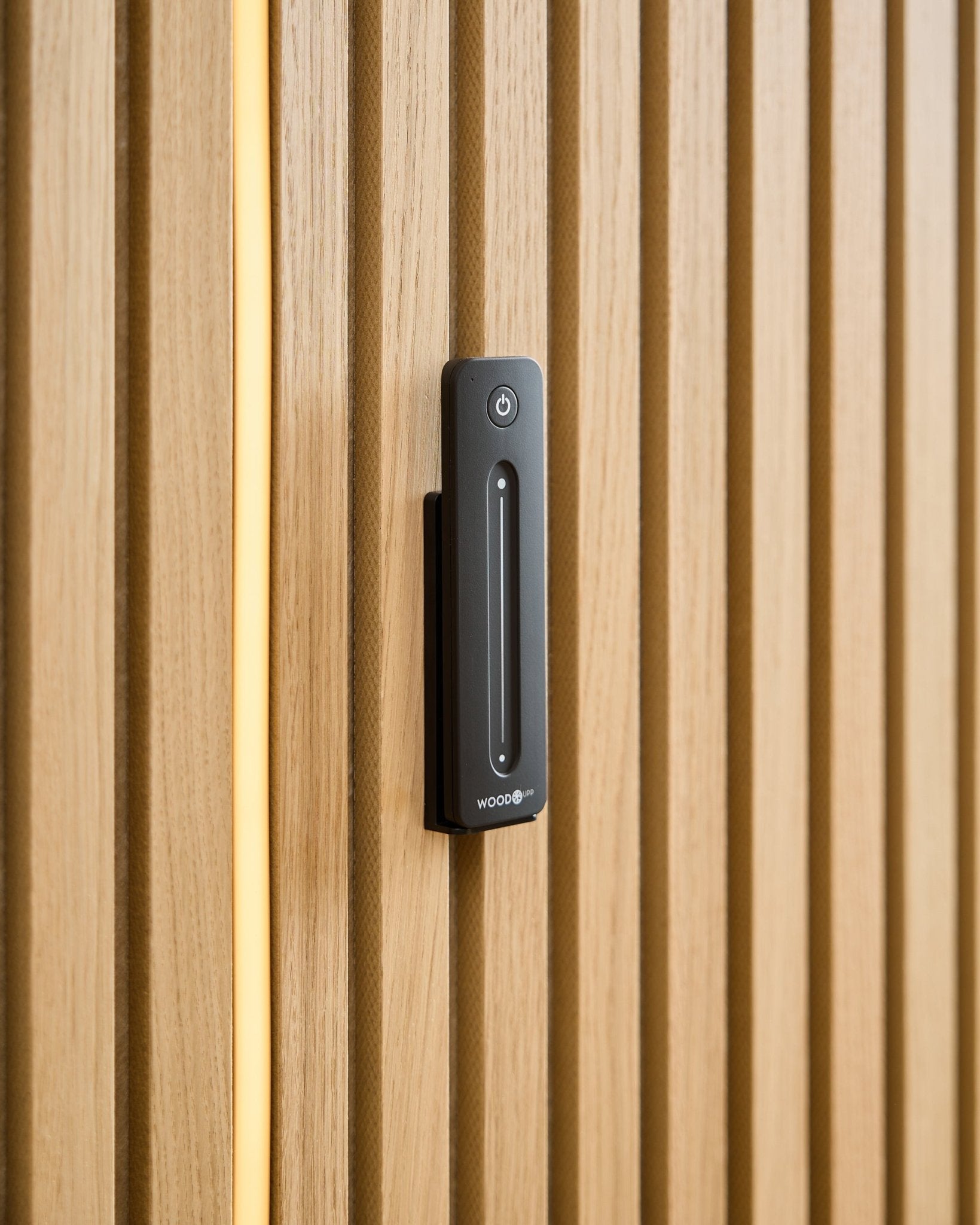 Un WoodUpp Lumi | Remote / LED Striplight è installato su un Pannello acustico in legno chiaro, con un cavo giallo visibile dietro le doghe in legno.