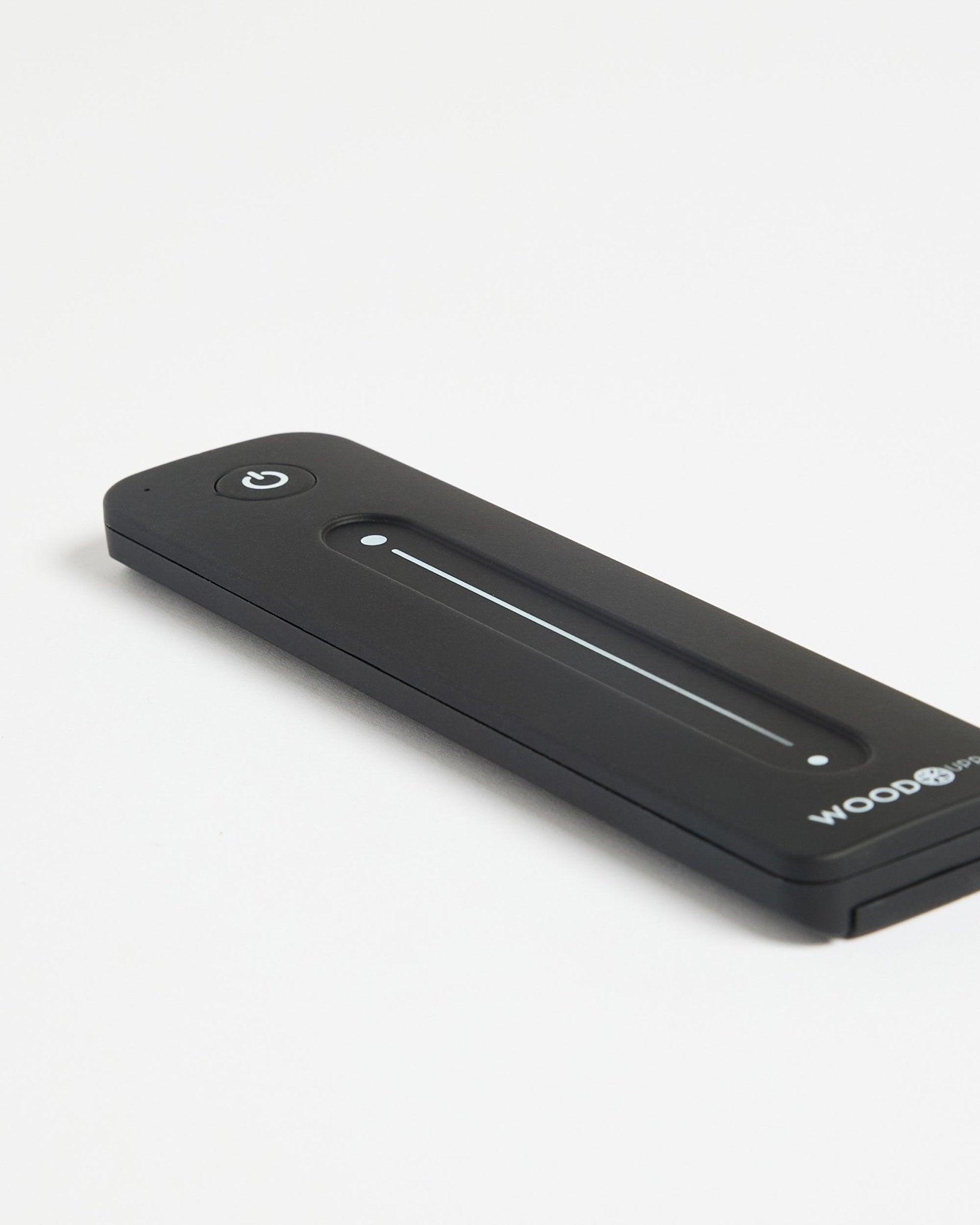 Telecomando WoodUpp Lumi per strip LED in black, con pulsante di accensione, compatibile con Philips Hue, mostrato su una superficie bianca.