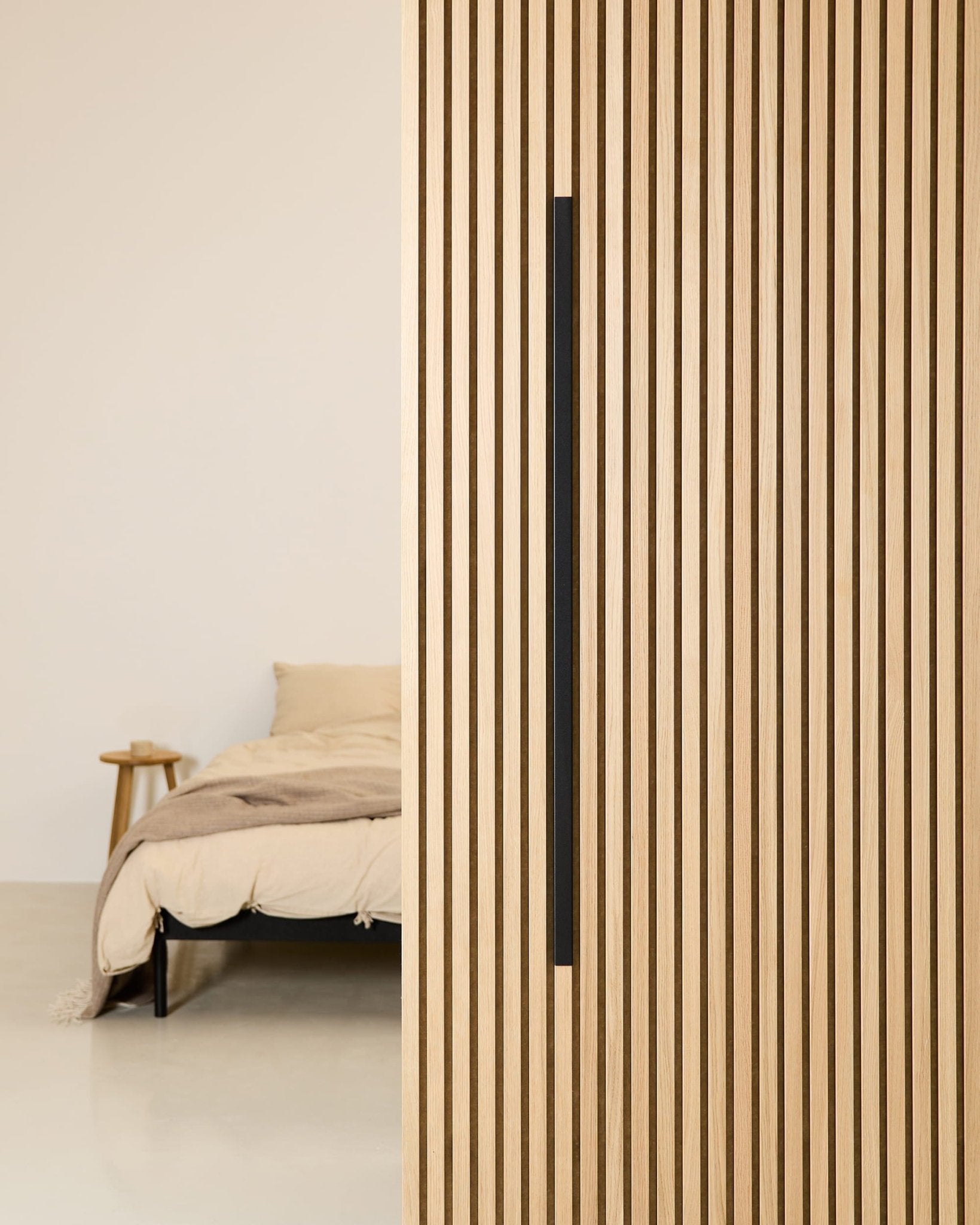 Camera da letto in stile minimalista con un letto beige, un comodino in legno e un pannello acustico WoodUpp Akupanel Black Aluminum da 120 cm montato sulla parete.