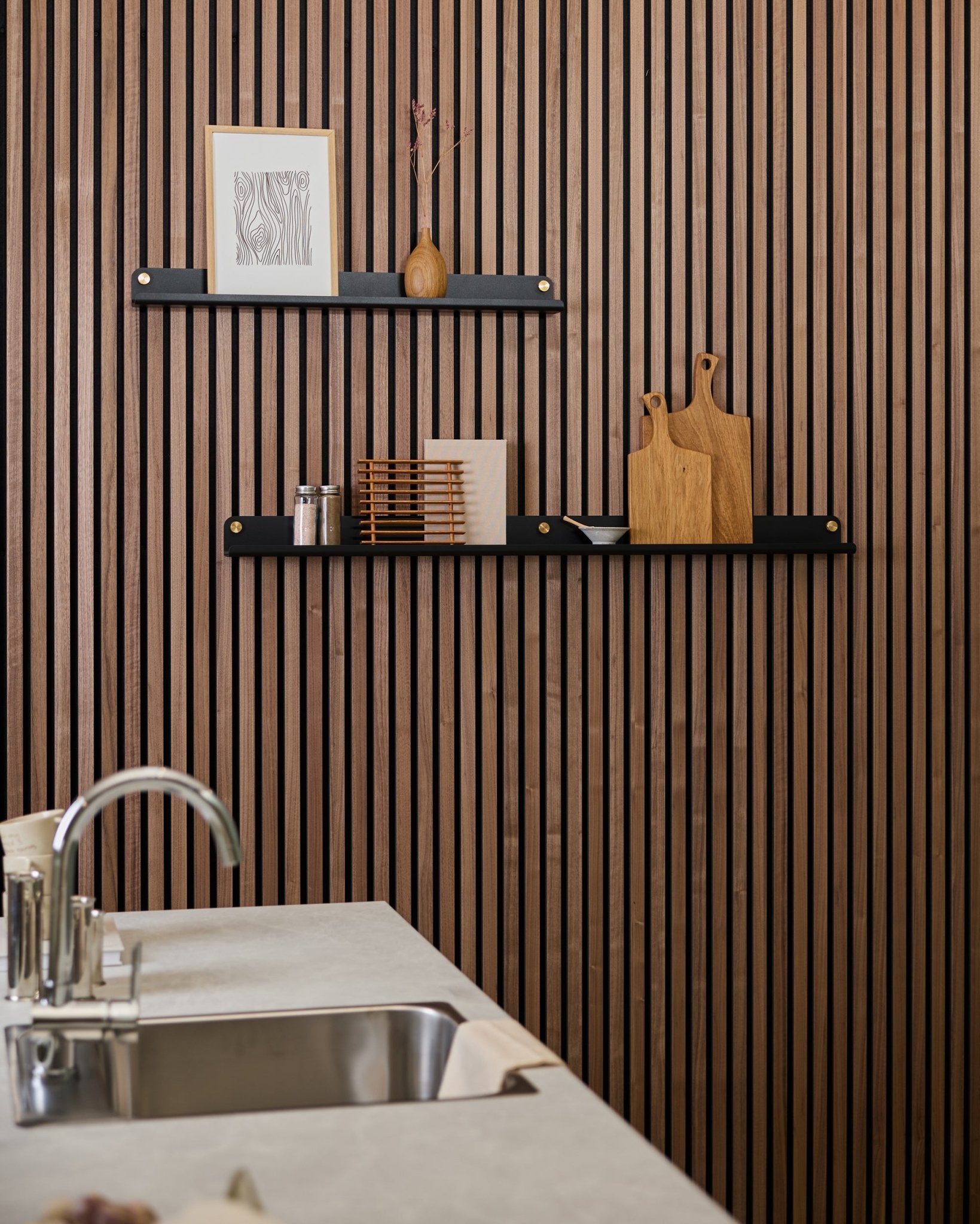 Cucina minimalista con una parete acustica in doghe di legno Akupanel vertical, mensole black, taglieri, elementi decorativi small e un moderno piano con lavello davanti.