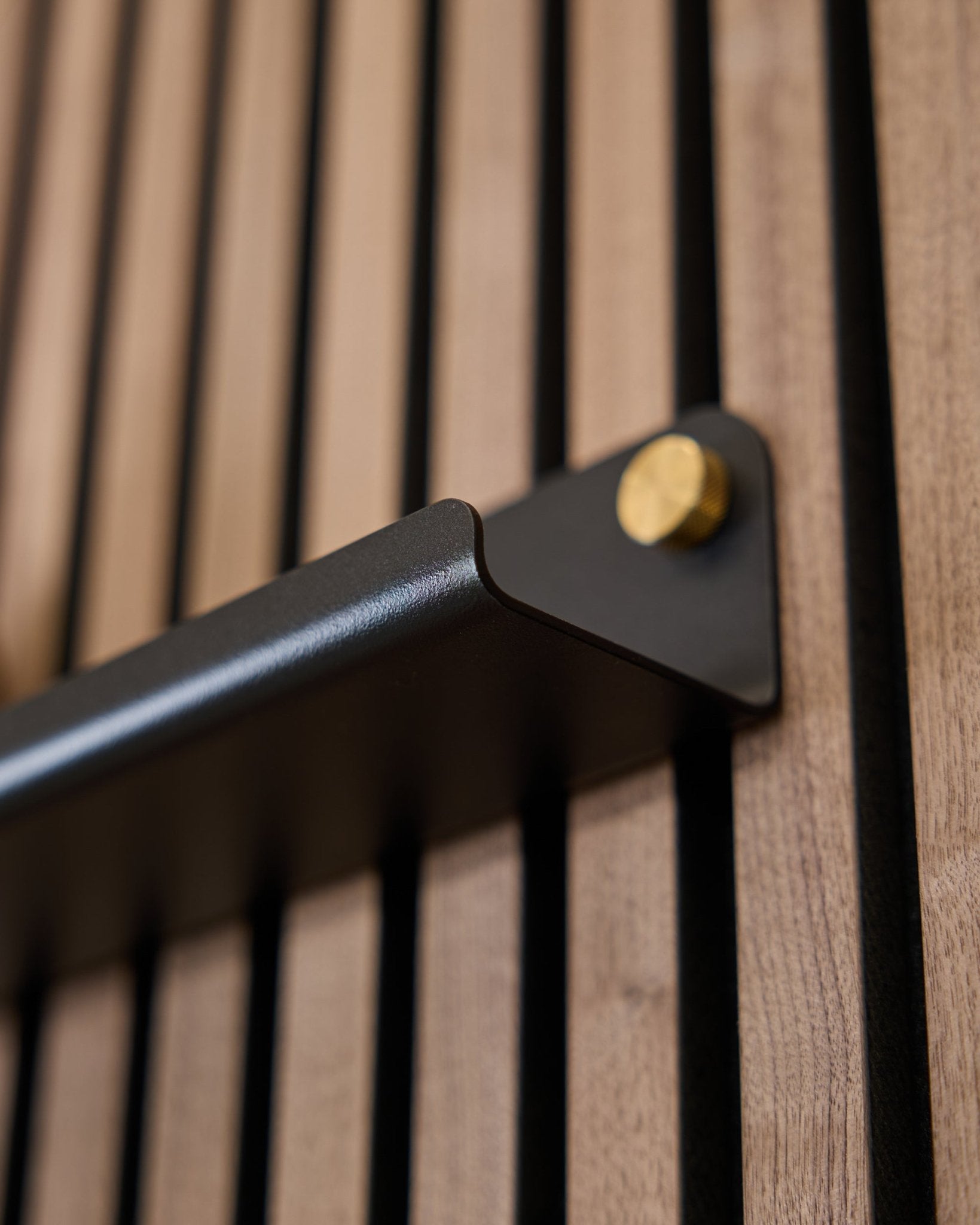 Primo piano di Norr | Narrow Shelf (75,9 cm) di WoodUpp in black, con maniglia in steel con bulloni dorati e superficie acustica scanalata in verticale.