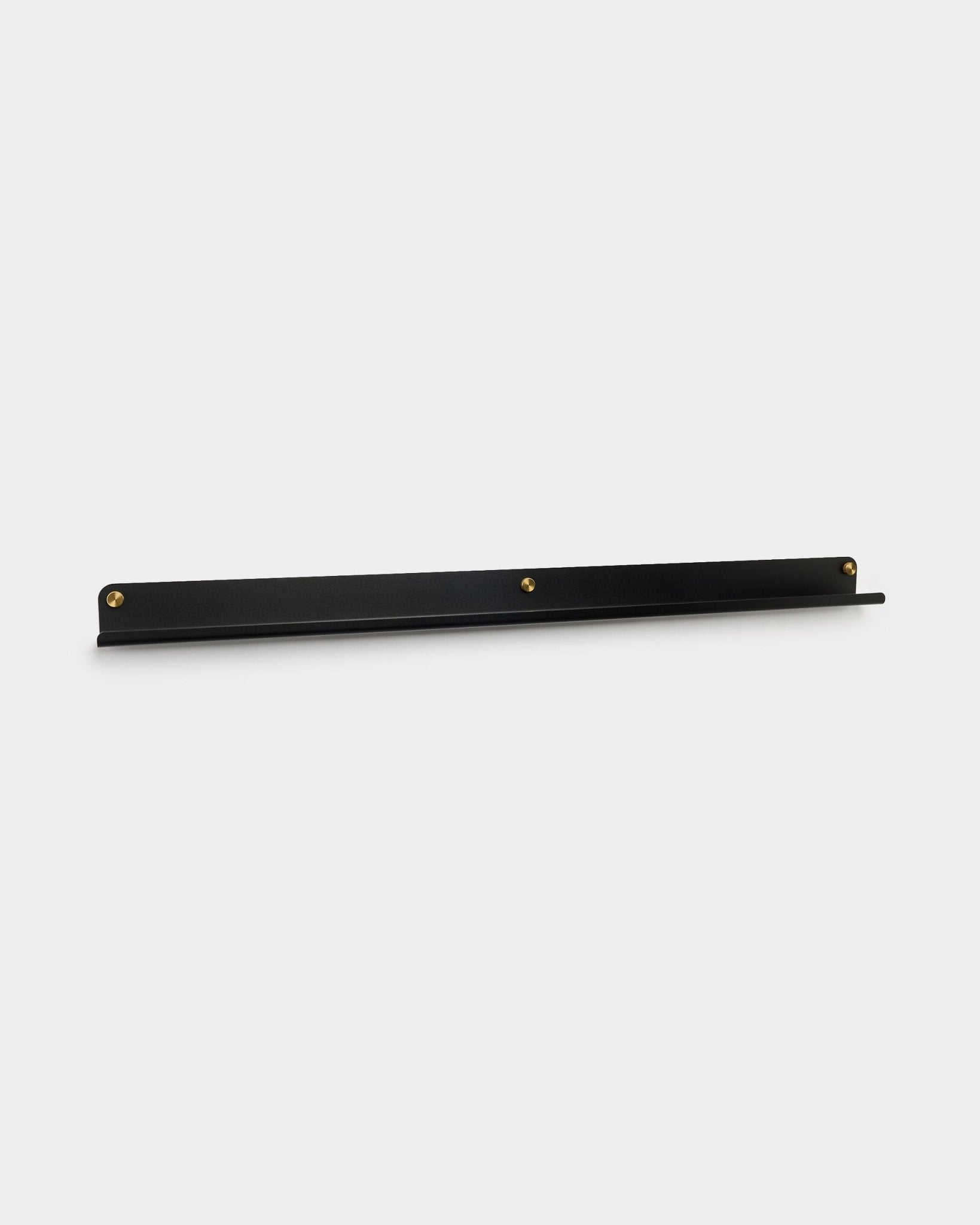 La mensola stretta Norr in black di WoodUpp, 115,9 cm, montata a parete con tre viti zigrinate brass, mostrata su uno sfondo bianco semplice.