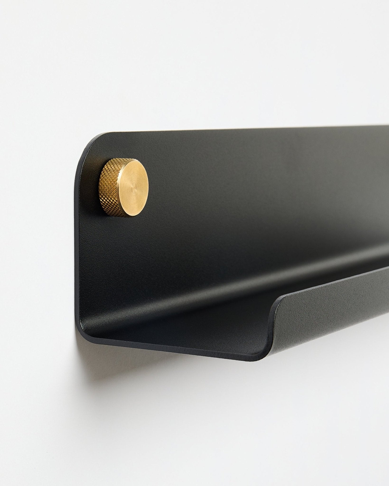 La Norr | mensola stretta in black (115,9 cm) con un singolo pomello dorato a sinistra, di WoodUpp, montata su una parete bianca semplice.