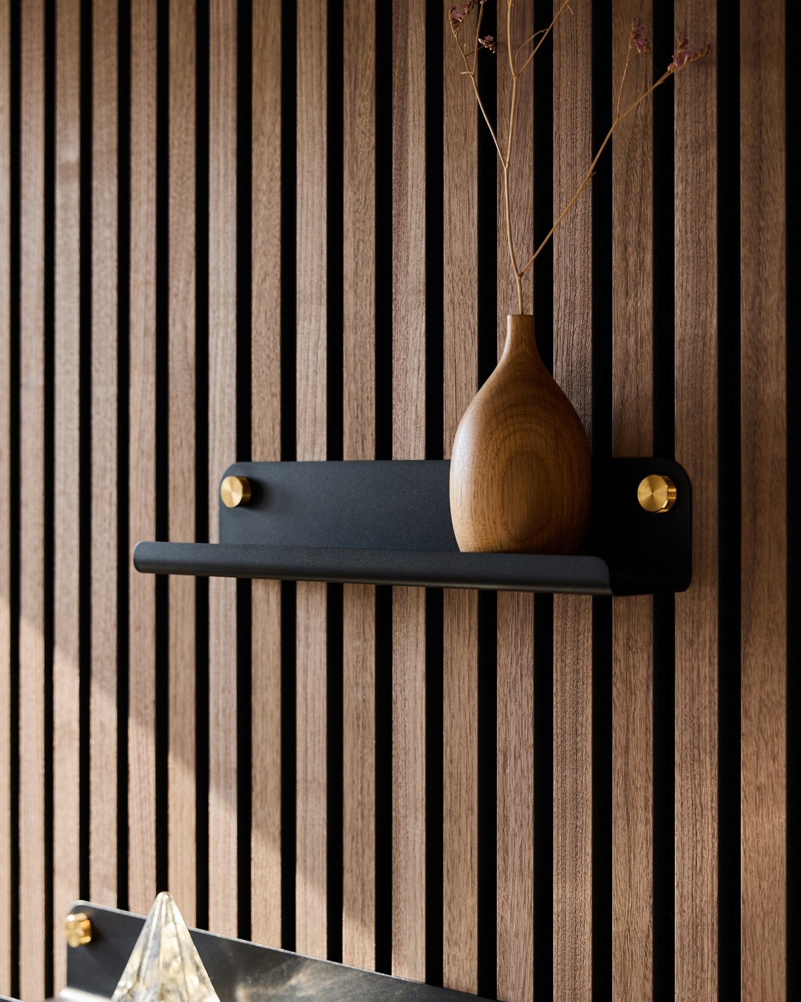 Un vaso in legno con rami secchi su una mensola stretta WoodUpp Norr black (35,9 cm), inserita in un pannello acustico a doghe in stile nordico vertical.