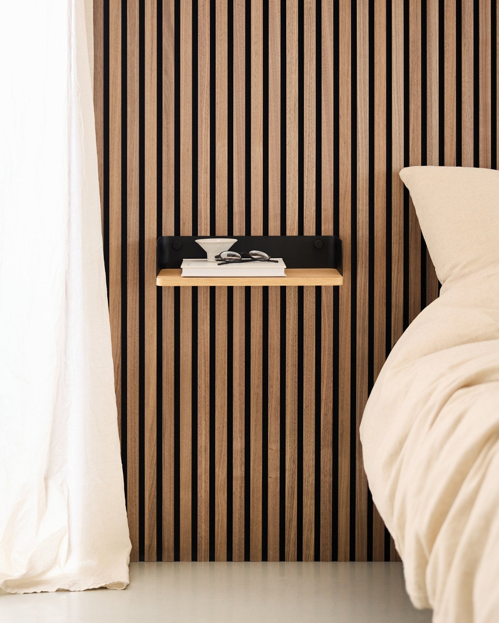 Camera da letto minimalista con parete a doghe in legno nordico Pannello acustico, libreria WoodUpp Linn in Natural Oak e comodino sospeso accanto a un letto beige.