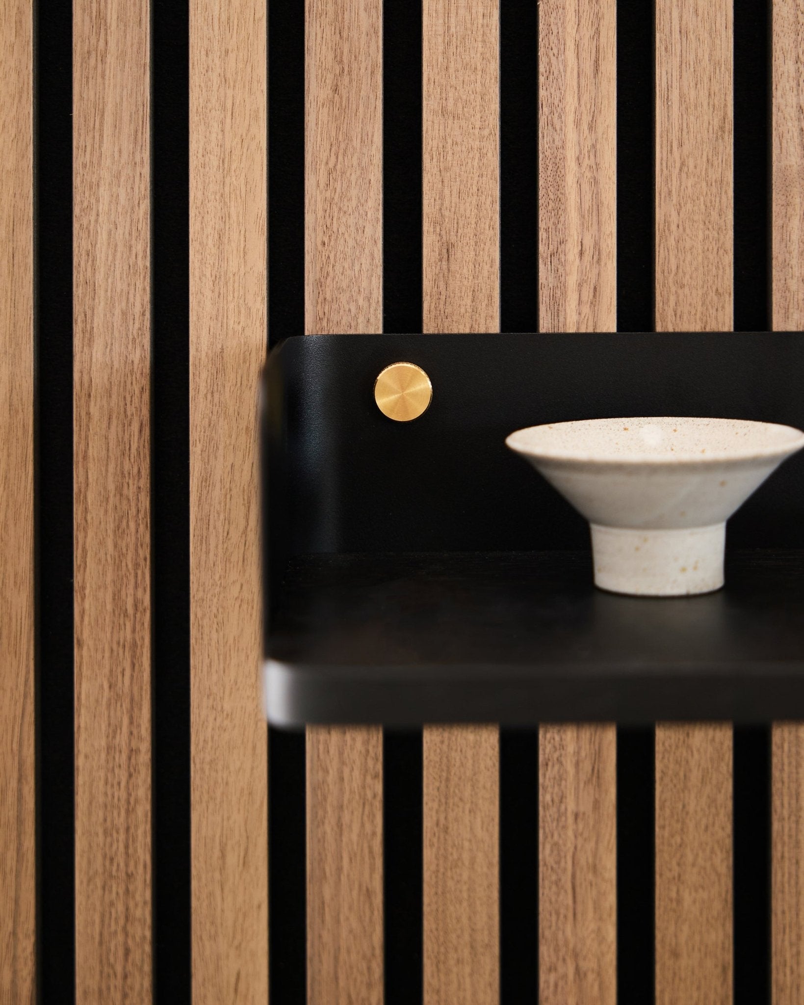Ciotola in ceramica appoggiata sulla libreria Linn di WoodUpp, 39,9 cm in black oak con doghe vertical black e un accento brass, in linea con il design minimalista nordico.