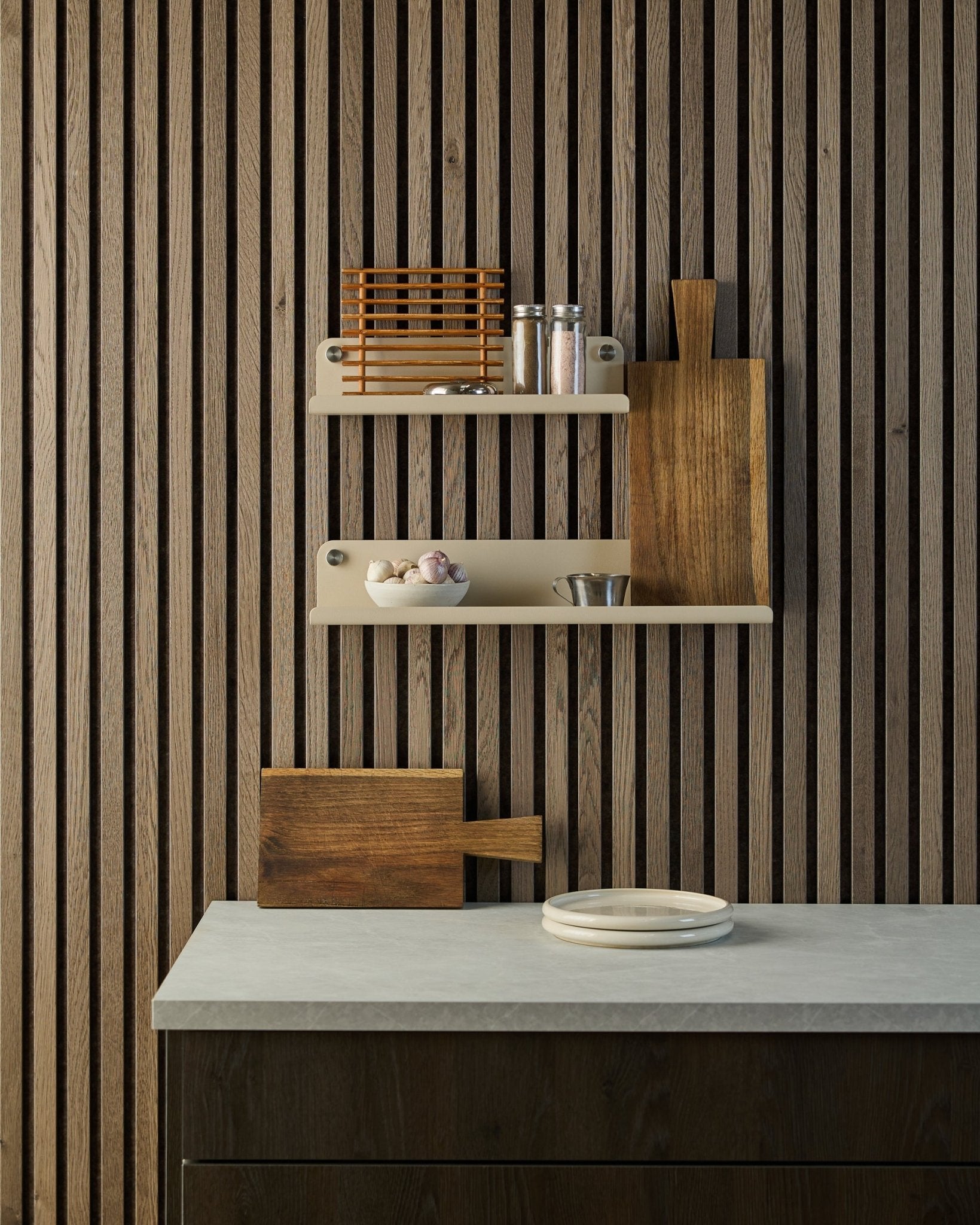 Cucina minimalista con parete acustica a doghe in legno Nordic Akupanel, mensole a giorno con spezie e ciotole, piano di lavoro con piatti bianchi e un tagliere.