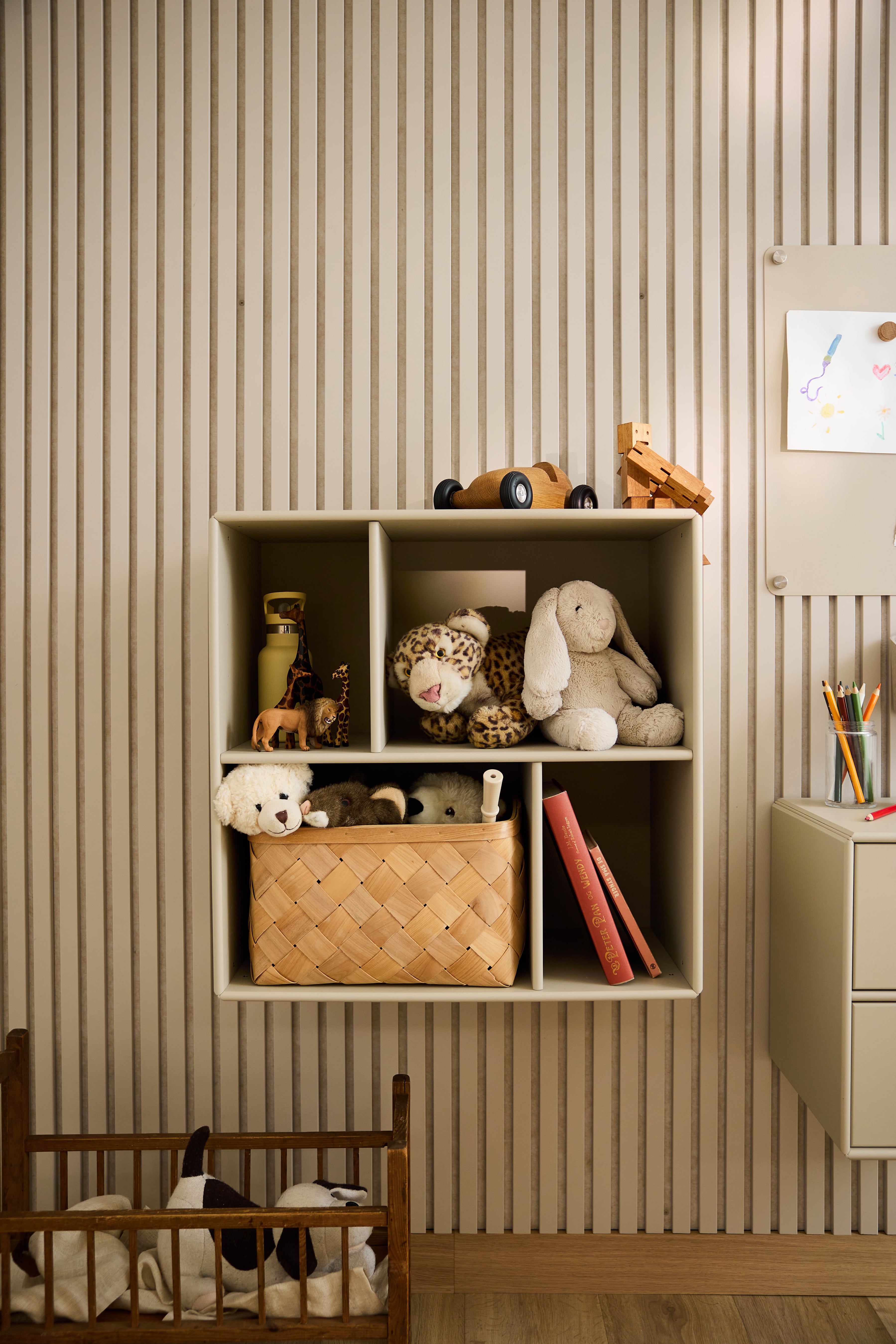 La credenza aperta WoodUpp Arka, di colore beige, con giocattoli e libri, che fa da contrappunto alla carta da parati a righe nella cameretta di un bambino, mette in risalto il design minimalista nordico.