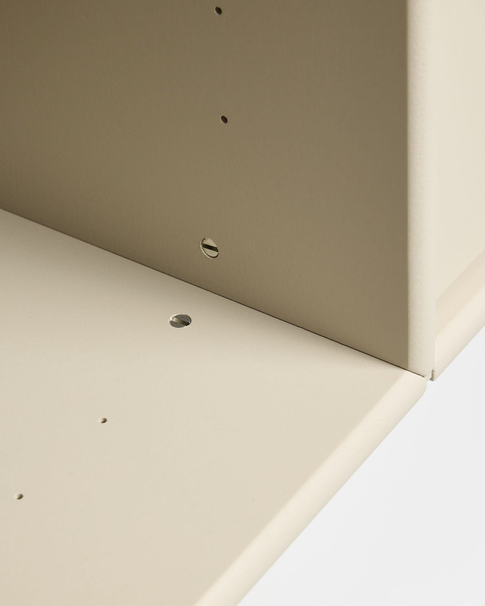 Primo piano di due pannelli beige della serie Arka TV Console di WoodUpp, uniti ad angolo retto con fori preforati per il montaggio modulare e la gestione dei cavi.