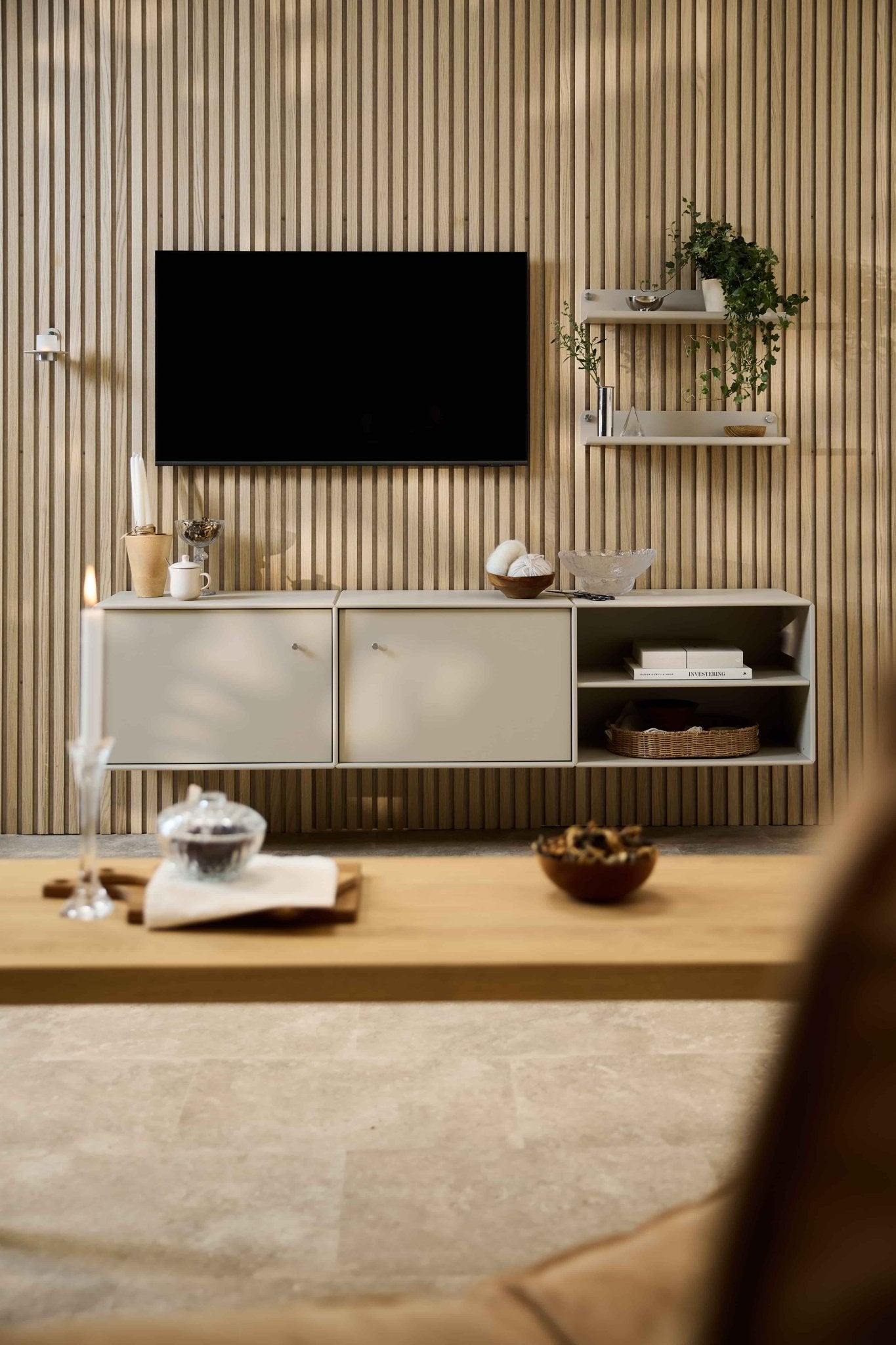 Soggiorno moderno con mobile TV Arka di WoodUpp, divani modulari, mensole in stile nordico con piante e oggetti decorativi, e una candela sul tavolino da caffè.