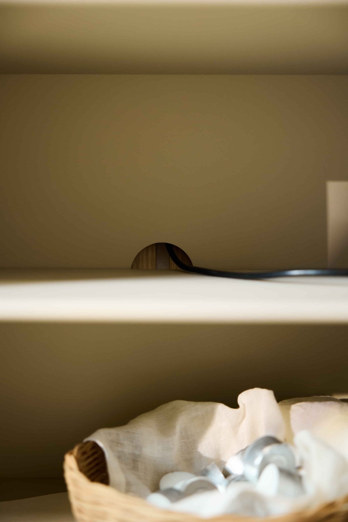 Primo piano del mobile TV Arka color beige di WoodUpp, illuminato da una luce soffusa, con un piccolo foro rotondo sul pannello posteriore per il passaggio dei cavi.