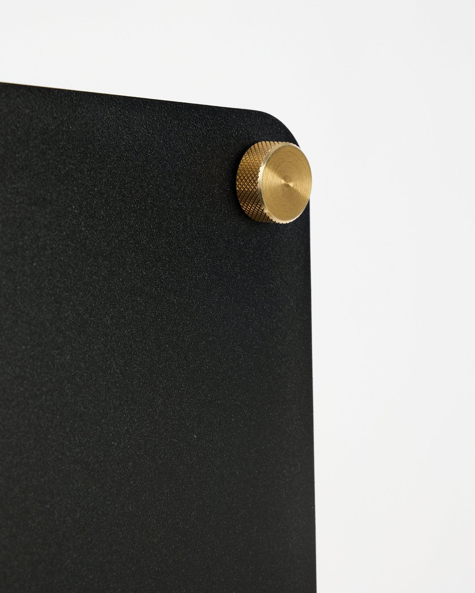 Primo piano della lavagna magnetica acustica WoodUpp Norr black (small) con angolo arrotondato e fissaggio con vite dorata su sfondo bianco.