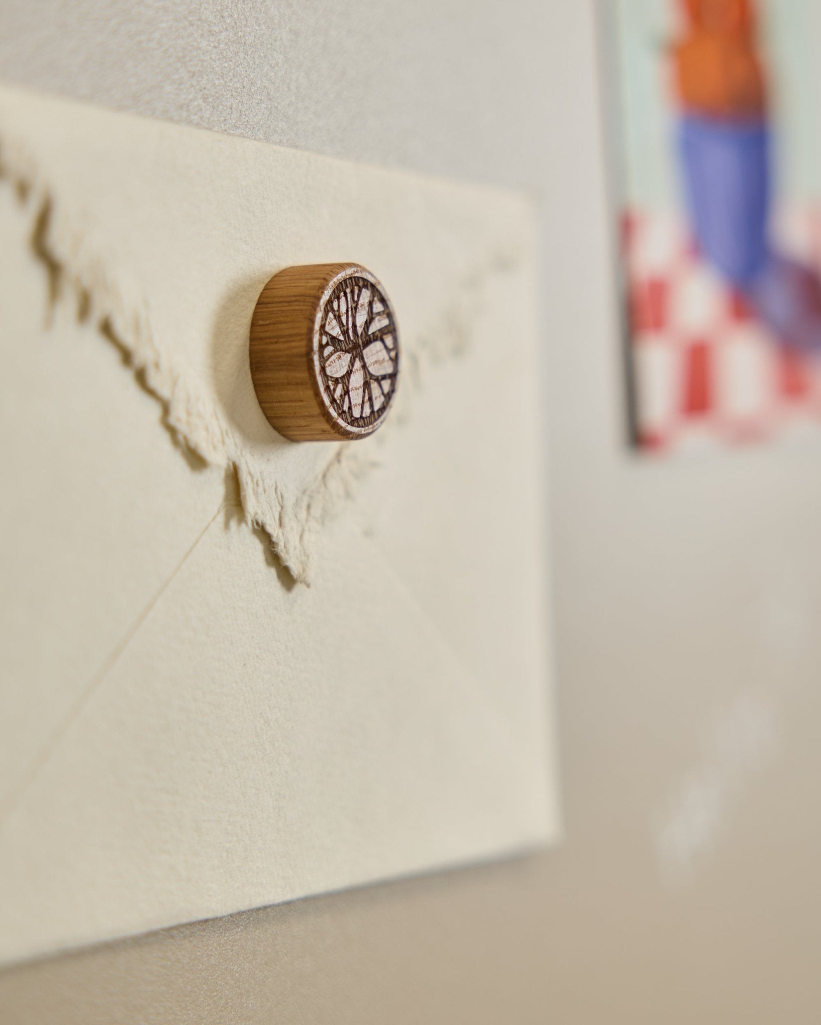 Una busta color crema è fissata a una Pannello acustico con un magnete WoodUpp Norr Natural Oak, caratterizzato da un motivo minimalista ad albero.