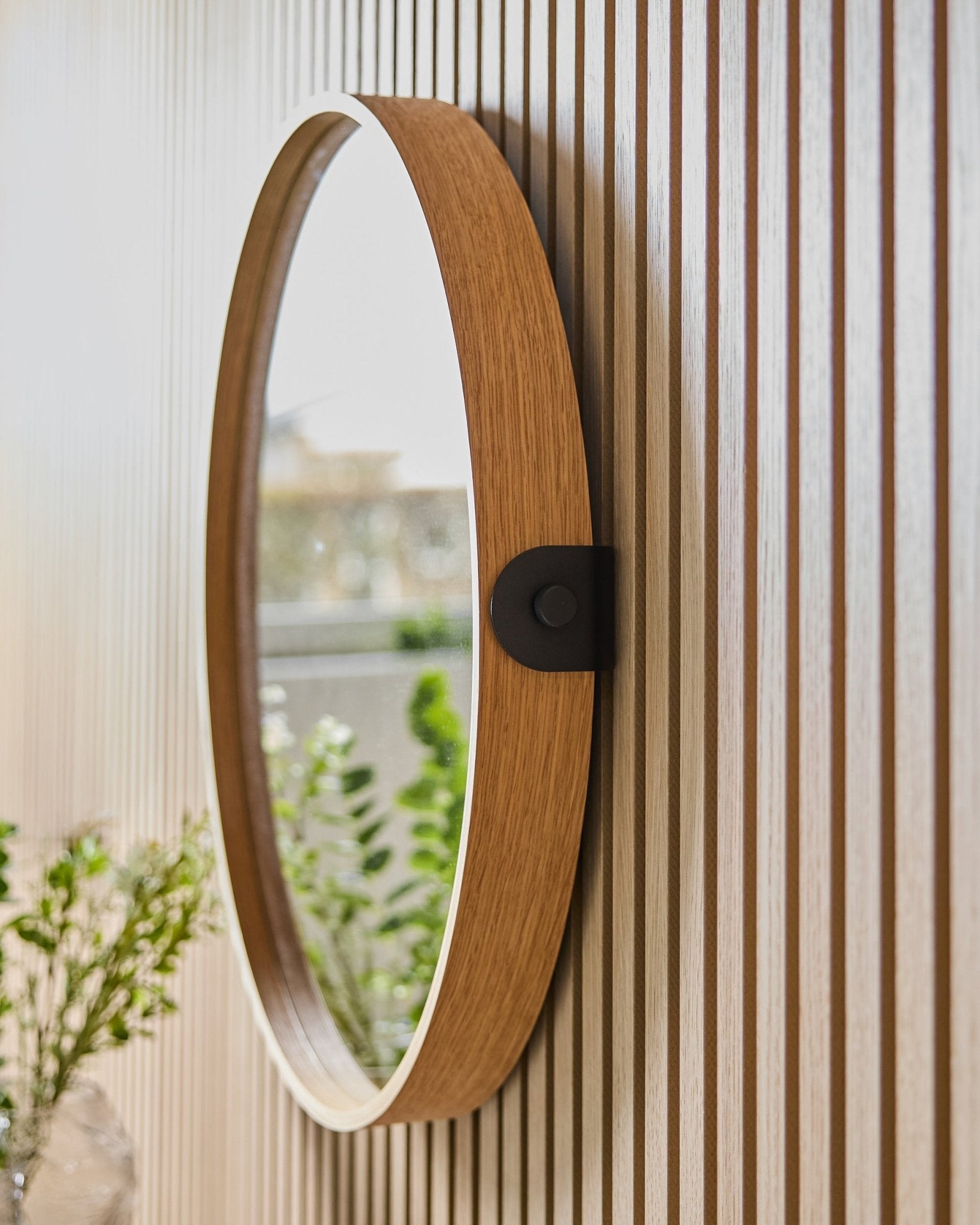 Linn | Mirror / Natural Oak di WoodUpp montato su una parete a righe Pannello acustico, che riflette il verde e la luce naturale provenienti da una finestra vicina.