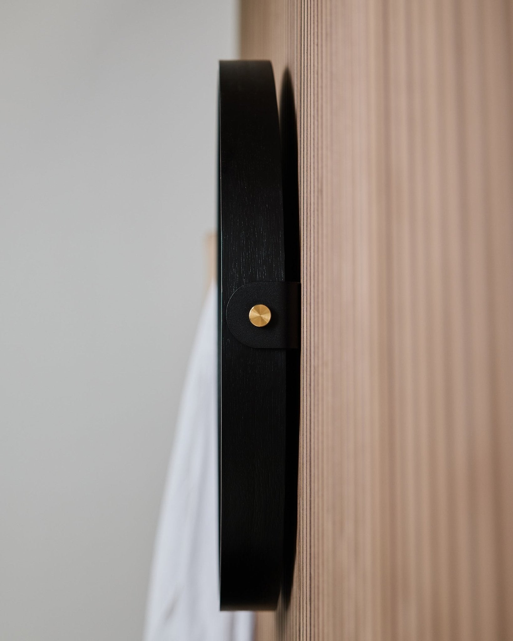 Primo piano laterale del gancio da parete WoodUpp Linn | Mirror / Black Oak, montato su un Rovere Pannello acustico scanalato, progettato per appendere uno specchio rotondo.