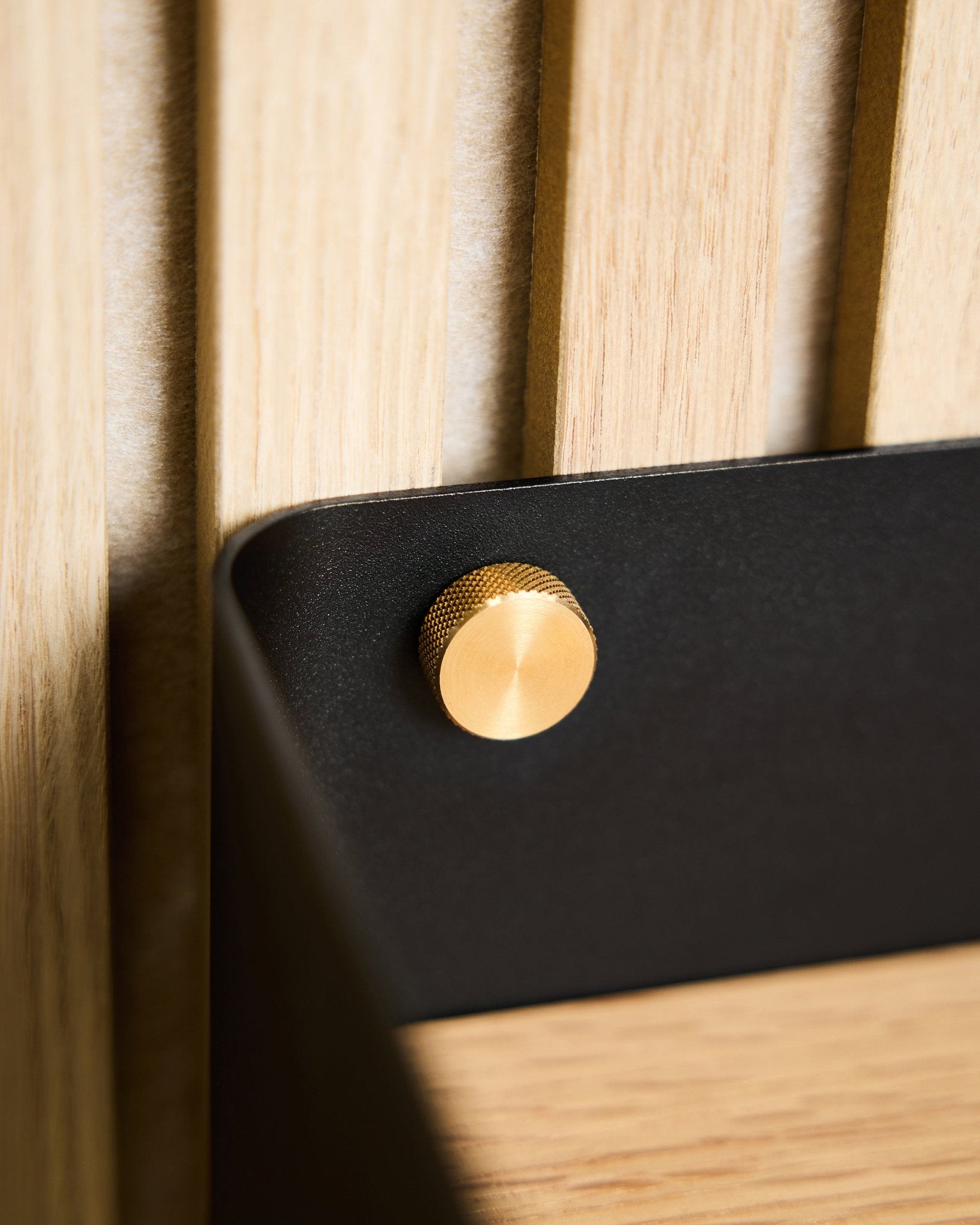 Primo piano di due viti zigrinate WoodUpp brass (M5x10 mm, 20x8.8), fissate a una staffa black montata su una superficie Pannello acustico in legno nordico chiaro.
