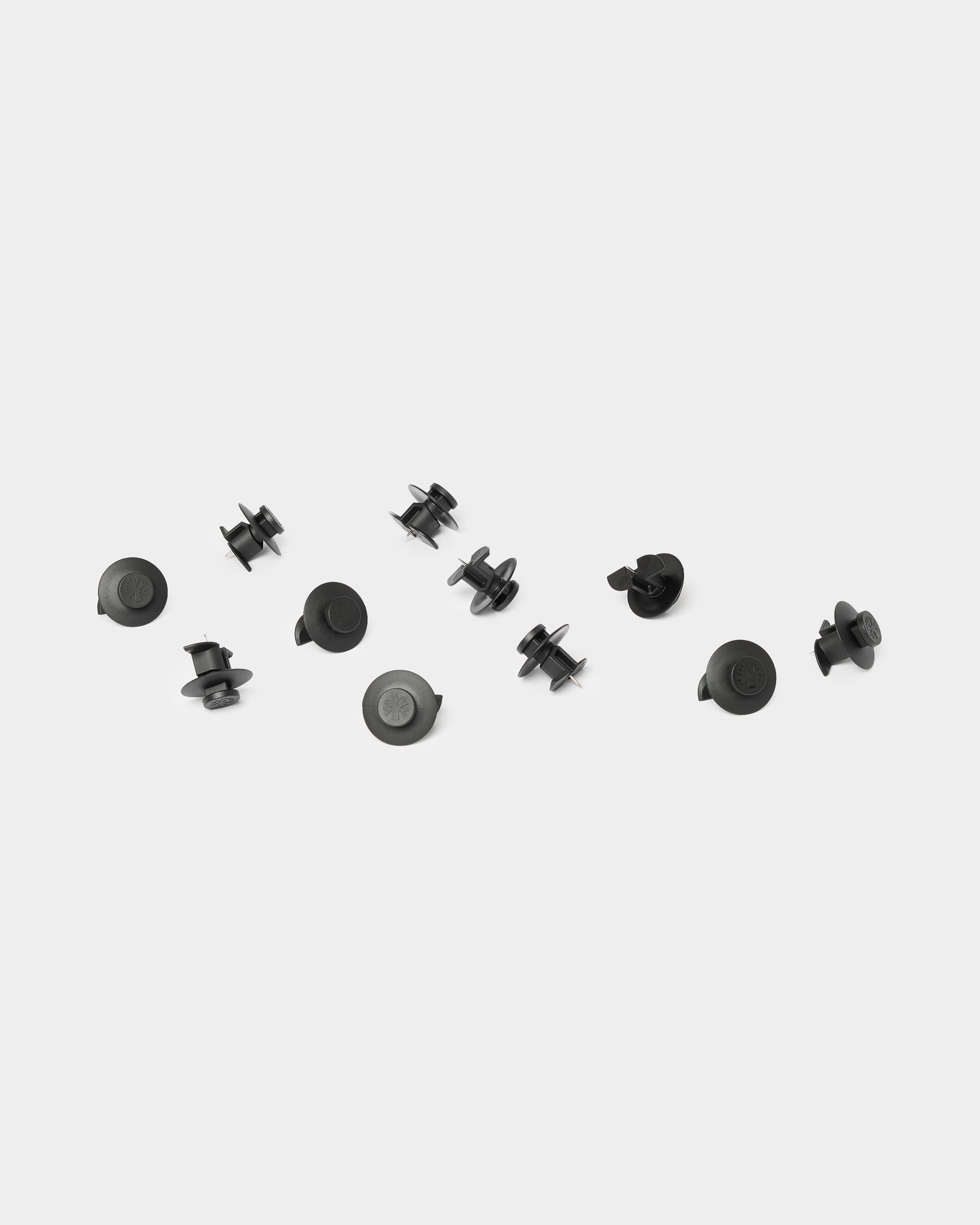 Dieci accessori WoodUpp Dupps di colore nero chiaro sono disposti su uno sfondo bianco a tinta unita, pensati per essere utilizzati con i pannelli acustici in legno Akupanel.