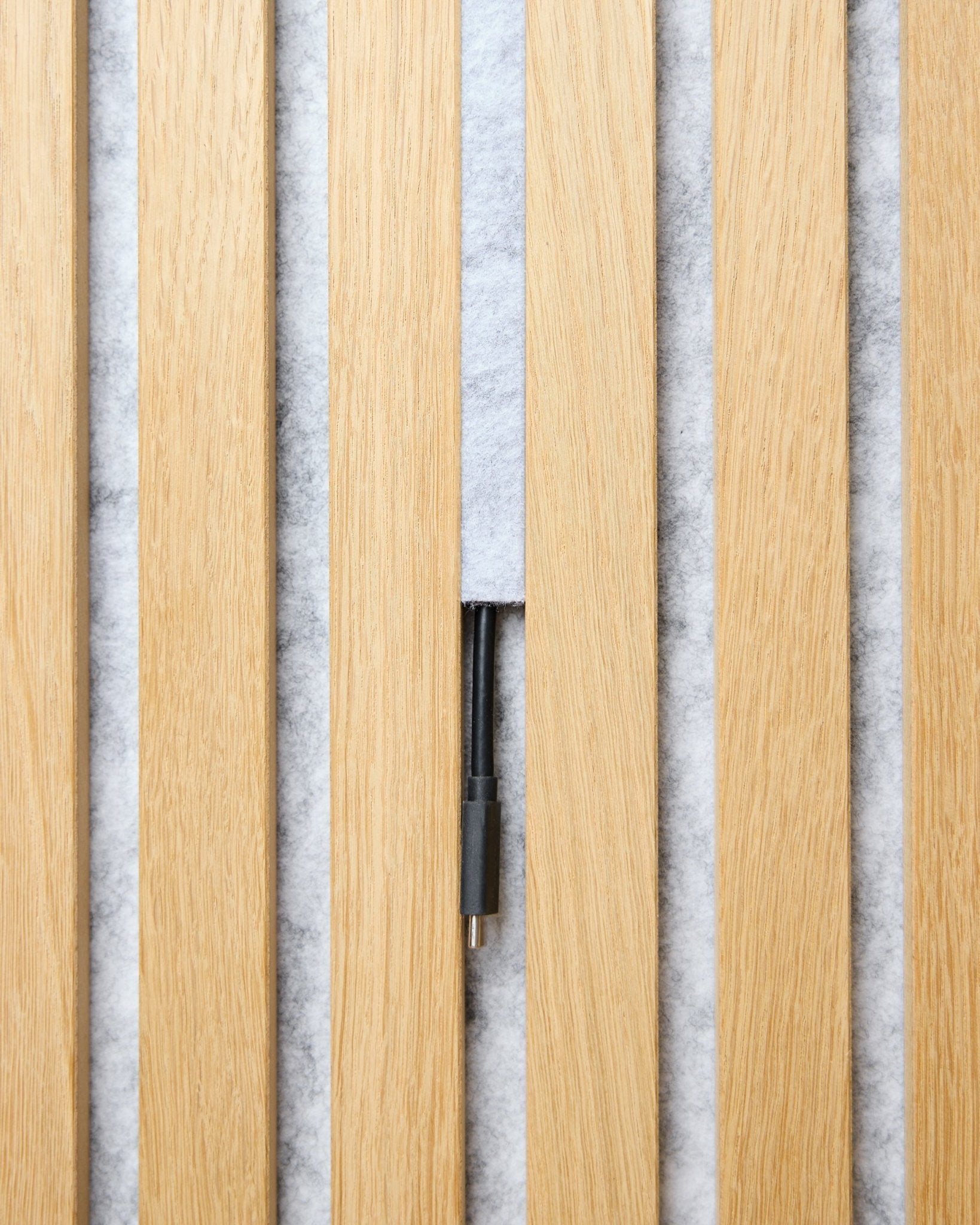 Il set Pop-on Cable Cover Dupps (grey, 3 pz) di WoodUpp organizza i cavi tra doghe acustiche in legno chiaro Akupanel su uno sfondo bianco testurizzato.