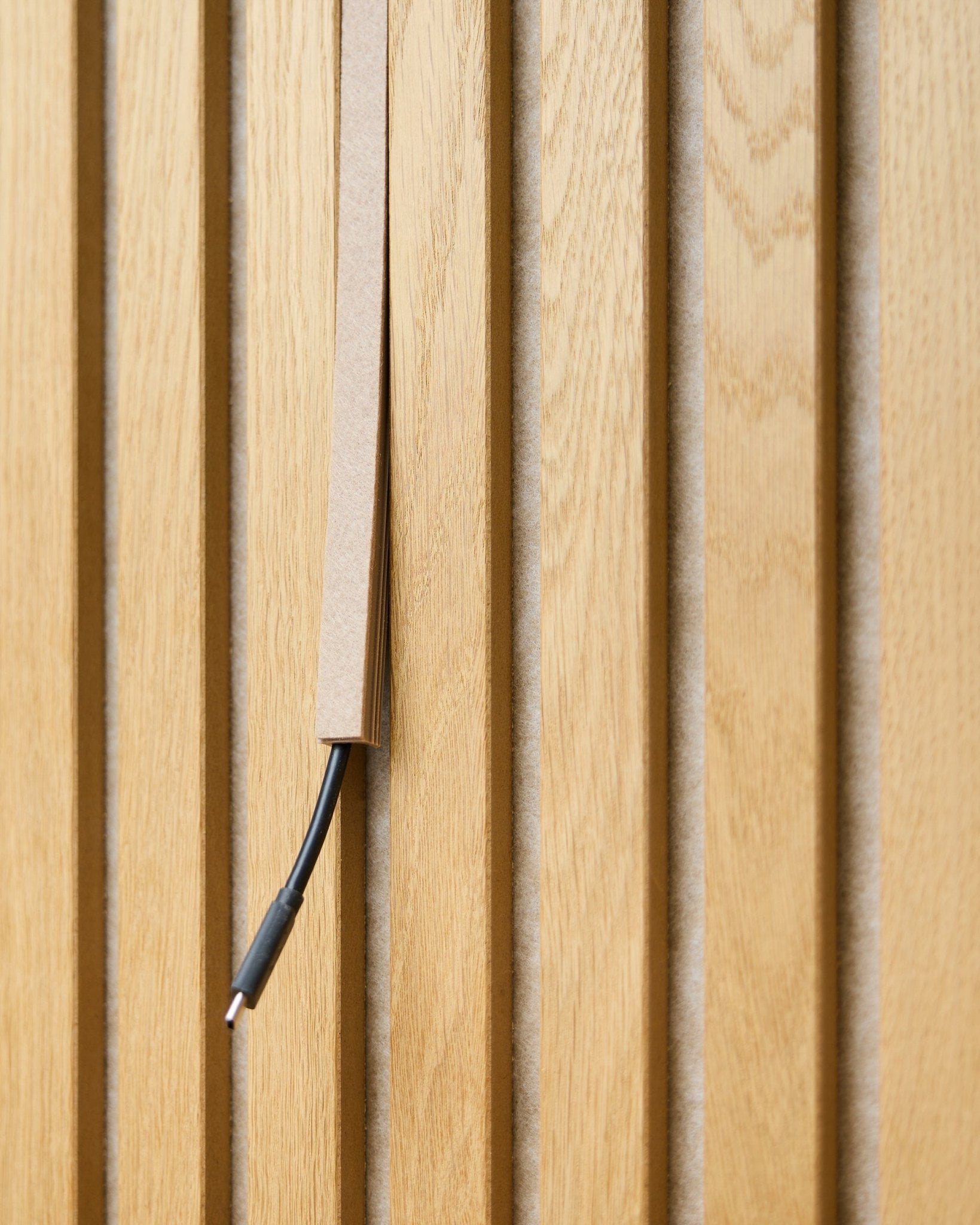 Un cavo black con sistema di gestione dei cavi è parzialmente nascosto in un copricavo Pop-on WoodUpp Dupps Beige, montato su doghe acustiche in legno vertical Akupanel.