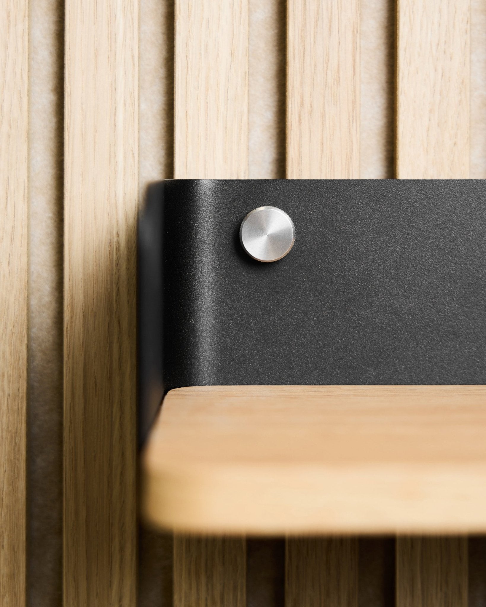 Primo piano di una mensola in legno chiaro con staffa in metallo black, montata con viti a testa zigrinata WoodUpp (M5x10 mm, in acciaio inox steel), abbinata a Nordic Pannello acustico.