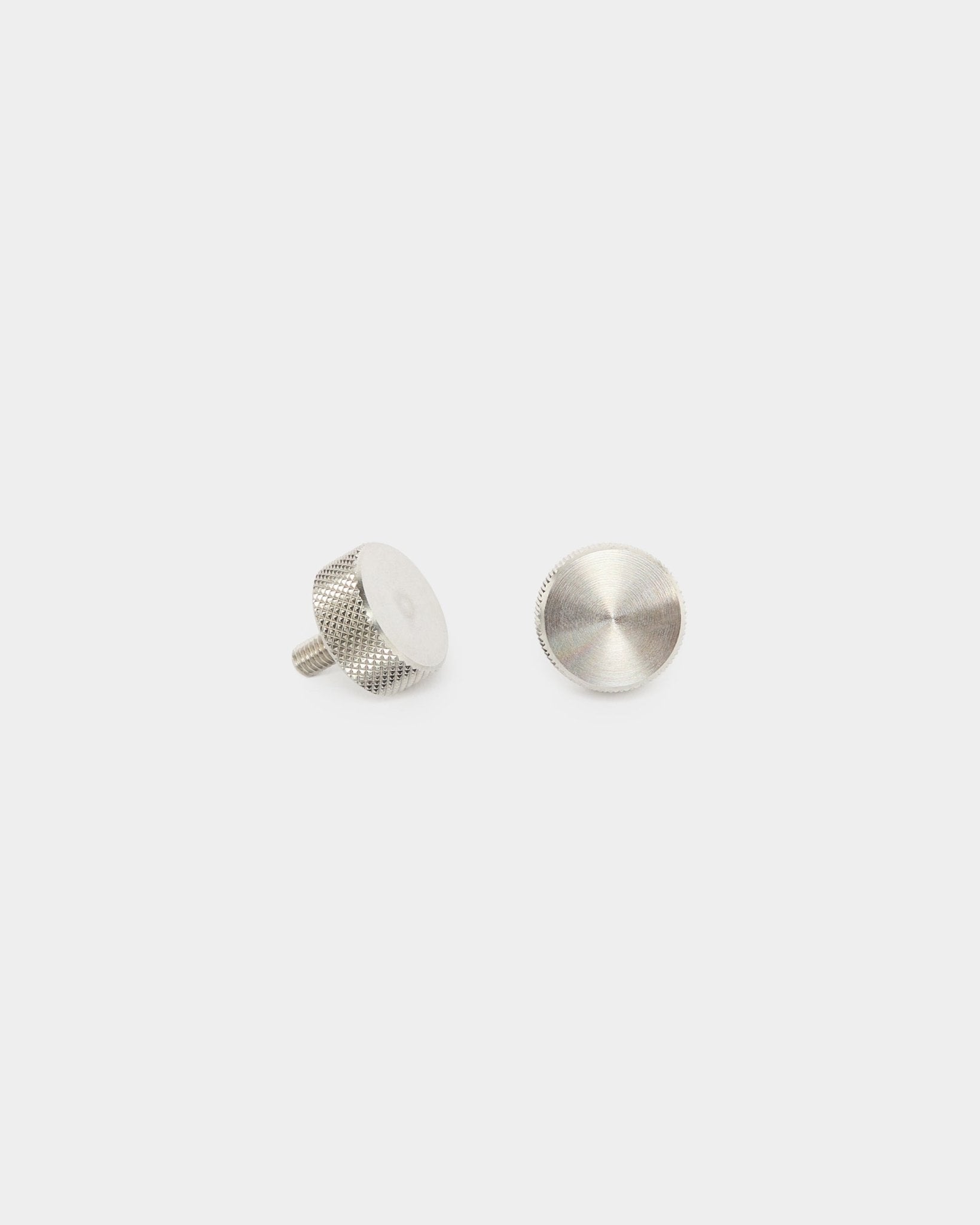 Due viti a testa zigrinata WoodUpp in acciaio inox steel (M5x10 mm, 20x8.8), accessori per pannelli acustici Akupanel, mostrate in posizione verticale e distesa su uno sfondo bianco semplice.