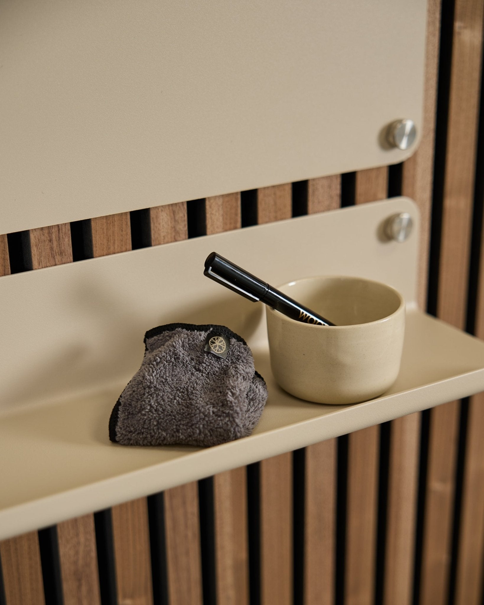Il set WoodUpp Norr Blackboard include una tazza small beige, una spazzola con manico black e un panno per la pulizia su una mensola beige con pannellatura acustica in legno in stile nordico.