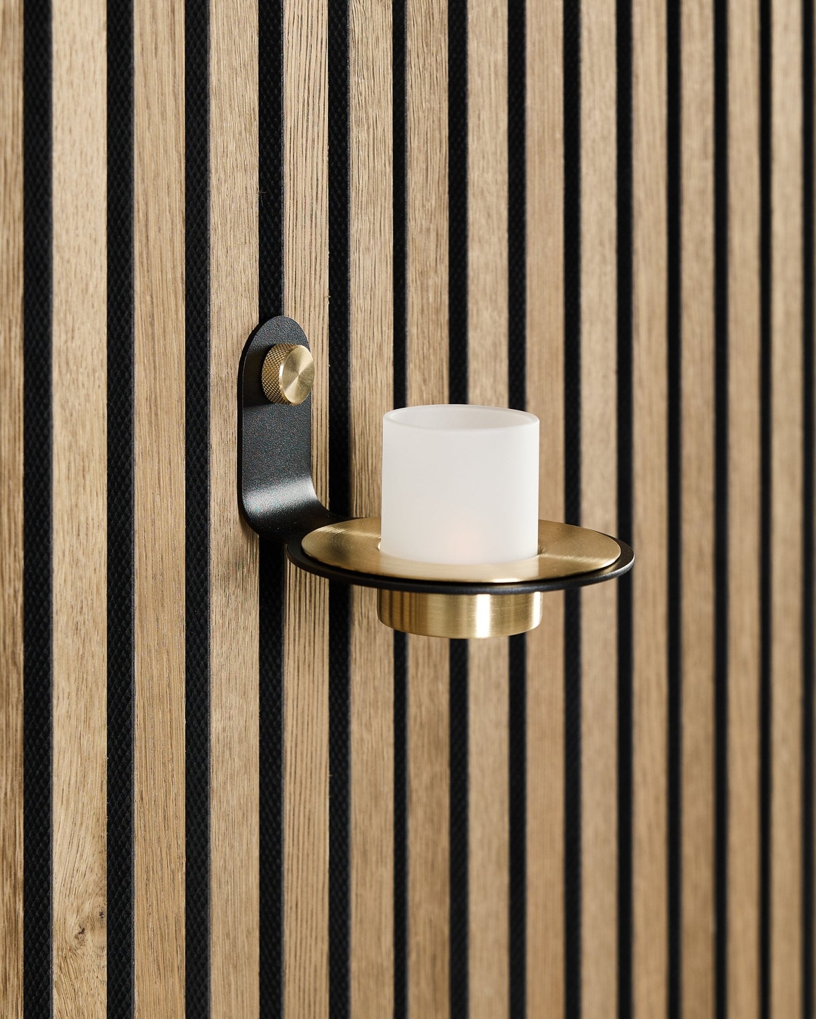 Il portacandela Norr in black e brass di WoodUpp è montato su un pannello acustico in legno nordico Akupanel con doghe black vertical.