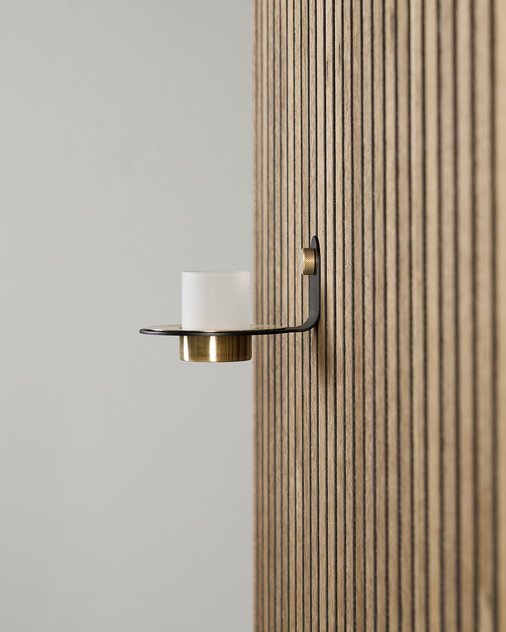 Portacandela Norr in black e brass di WoodUpp montato su un Akupanel vertical Pannello acustico, con vetro satinato e dettagli brass.