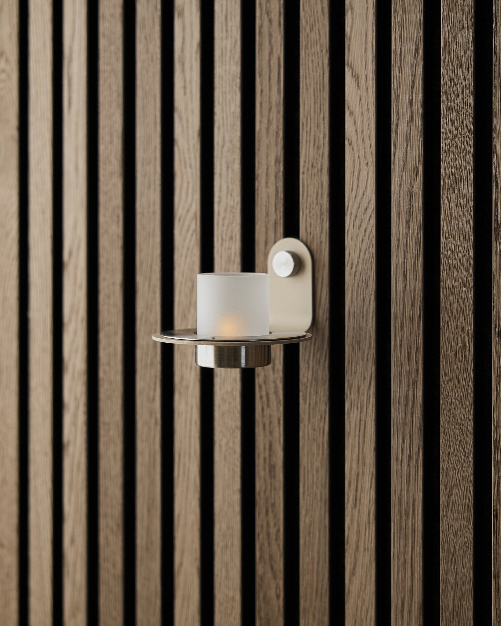 Il portacandele Norr in acciaio inox beige steel di WoodUpp, esposto su una parete beige Akupanel Pannello acustico.