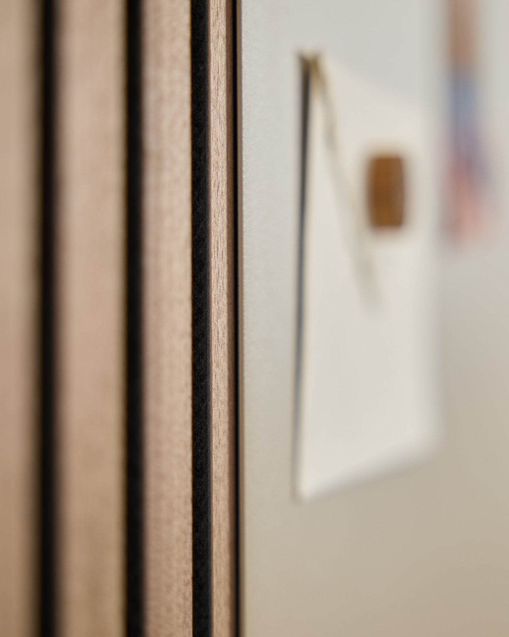 Primo piano di un pannello acustico in legno Akupanel di WoodUpp con doghe vertical, accanto a una lavagna magnetica large beige Norr sfocata sullo sfondo.