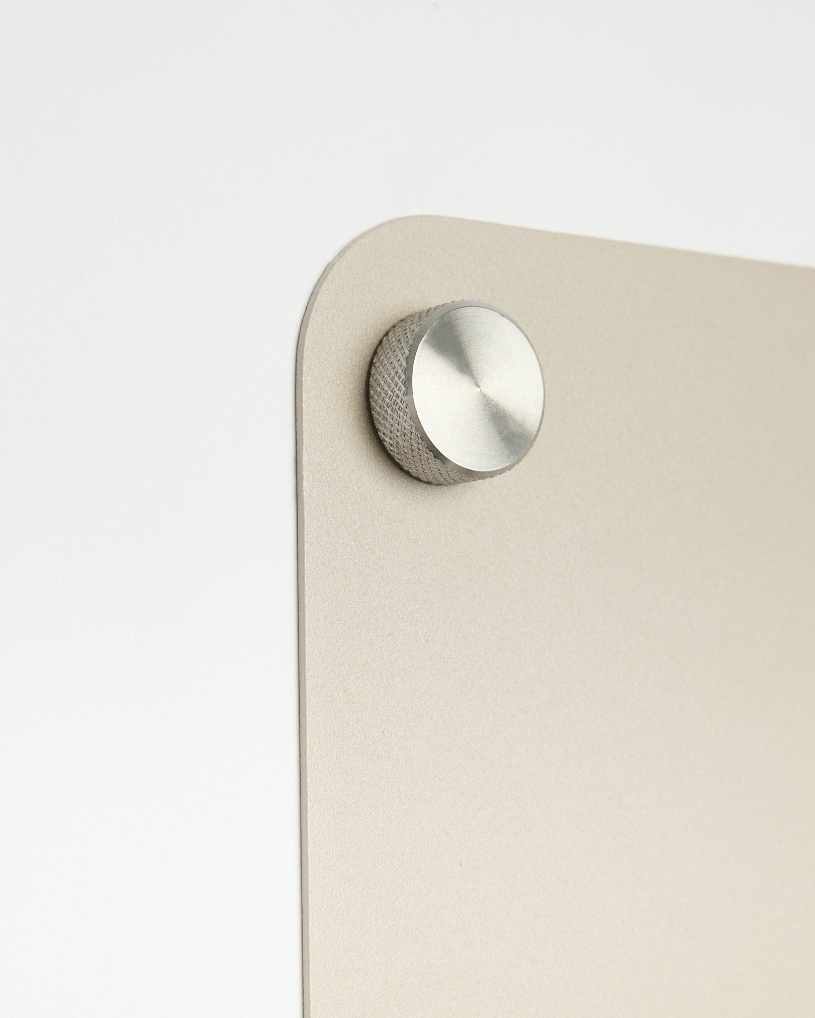 Primo piano di un accessorio con pomello rotondo in metallo fissato alla lavagna magnetica large beige Norr di WoodUpp, con dettaglio in vetro satinato su sfondo bianco.
