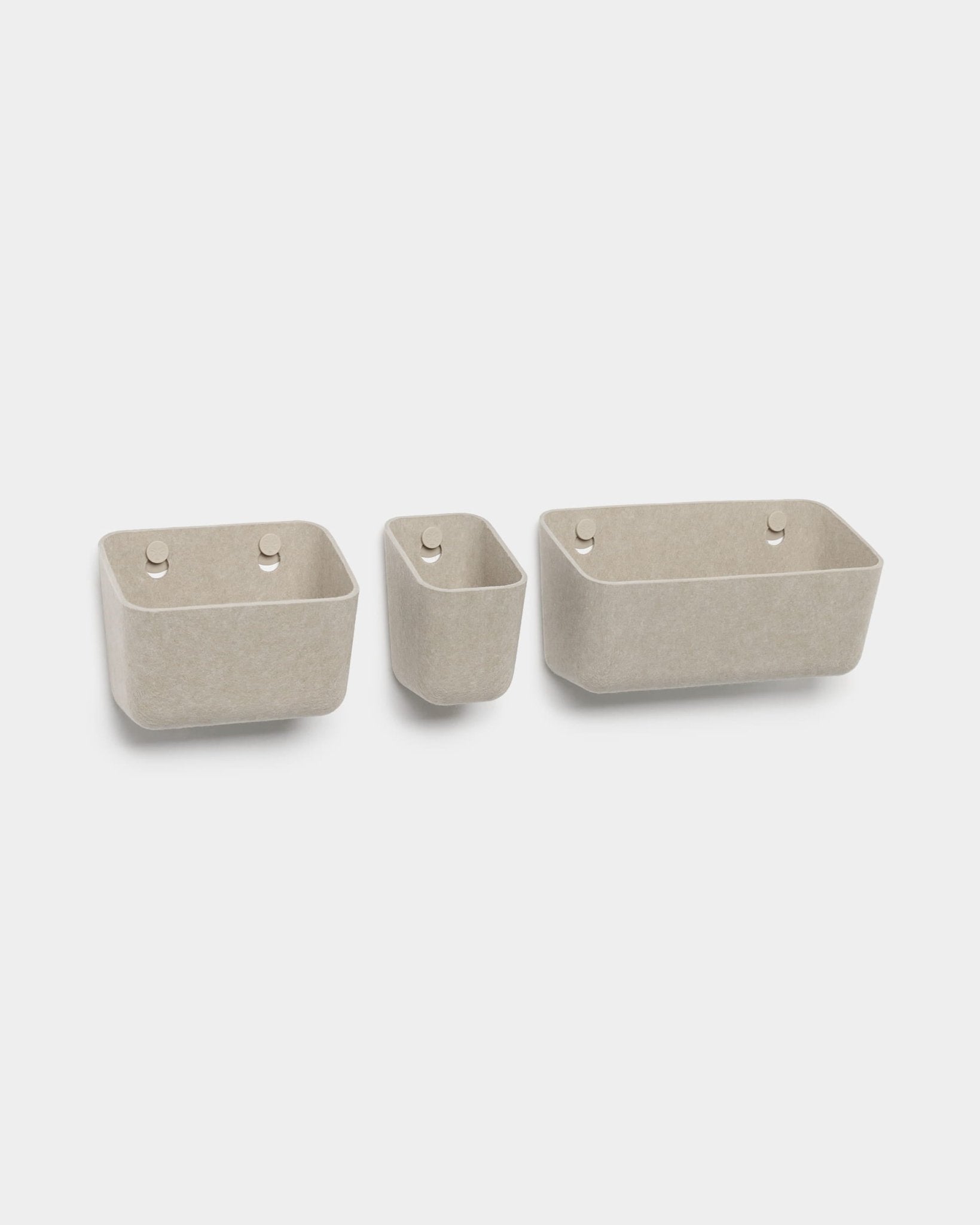 Set di tre contenitori in feltro WoodUpp Luva color beige, ciascuno con due fori rotondi per appenderli, raffigurati su sfondo bianco.