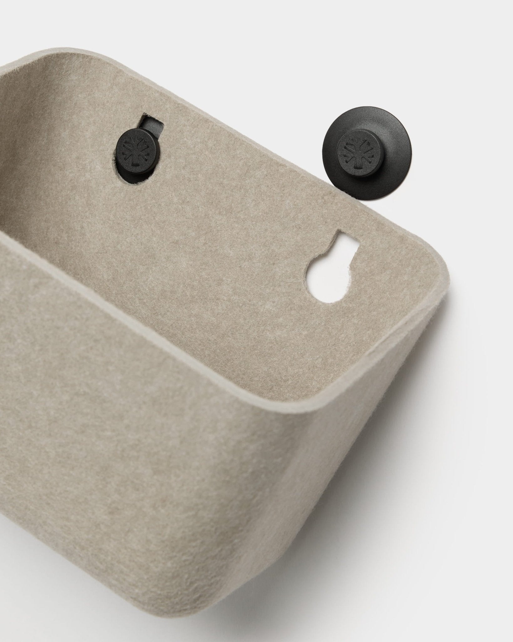 Accessorio da parete WoodUpp Luva in feltro beige con due staffe circolari nere; una delle staffe è raffigurata staccata e posizionata accanto al contenitore.