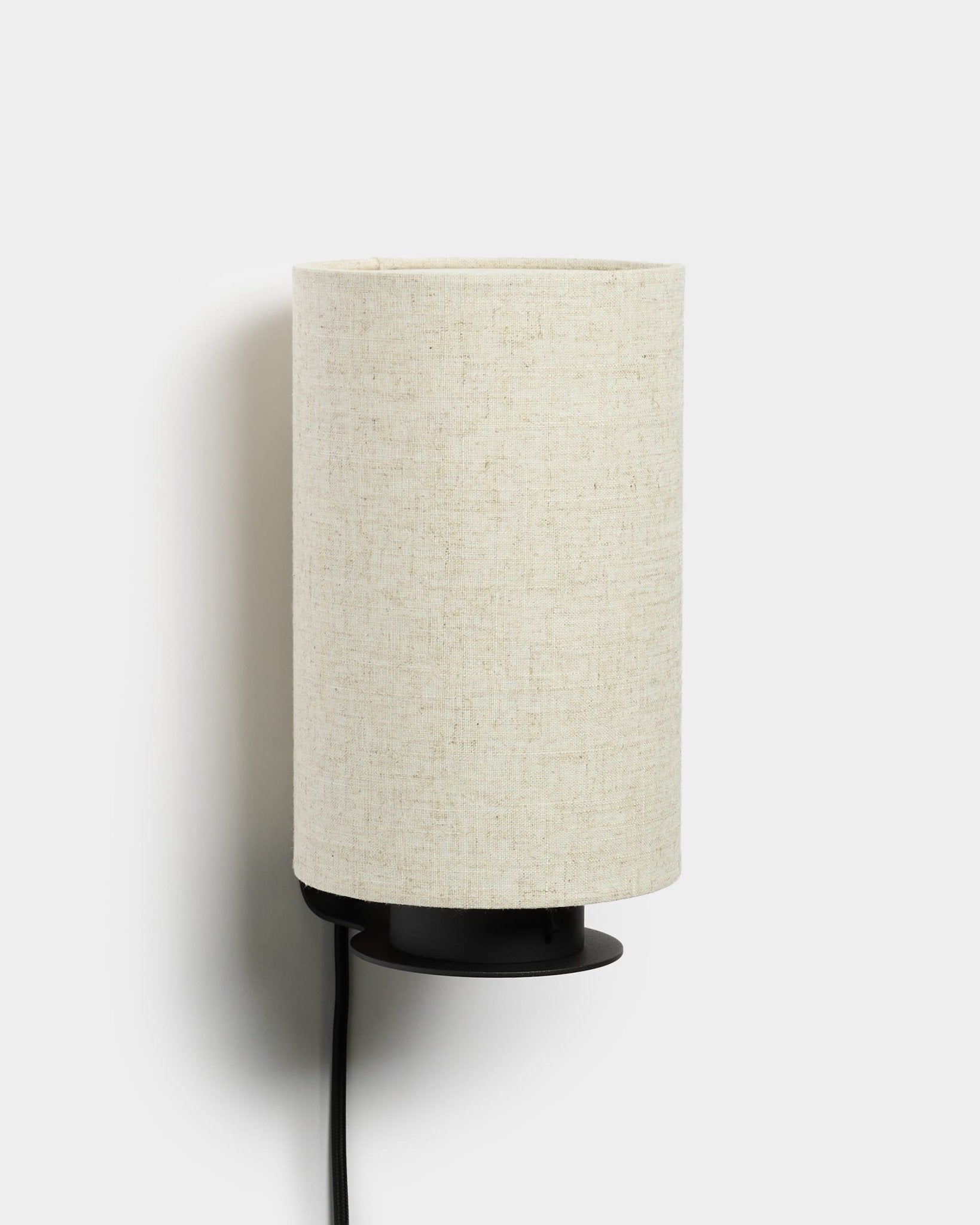 Lampada da parete Feya di WoodUpp con base in metallo black, paralume testurizzato in lino-cotone color beige e cavo di alimentazione a vista black. Design minimalista nordico.