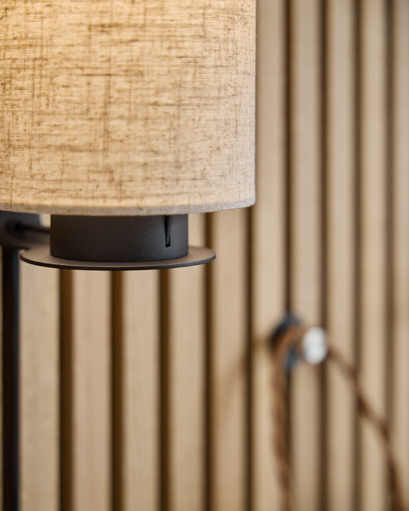Lampada da parete Feya / Black/Beige di WoodUpp con paralume in lino-cotone beige, base in metallo black e cavo a vista, montata su un pannello acustico nordico a doghe.