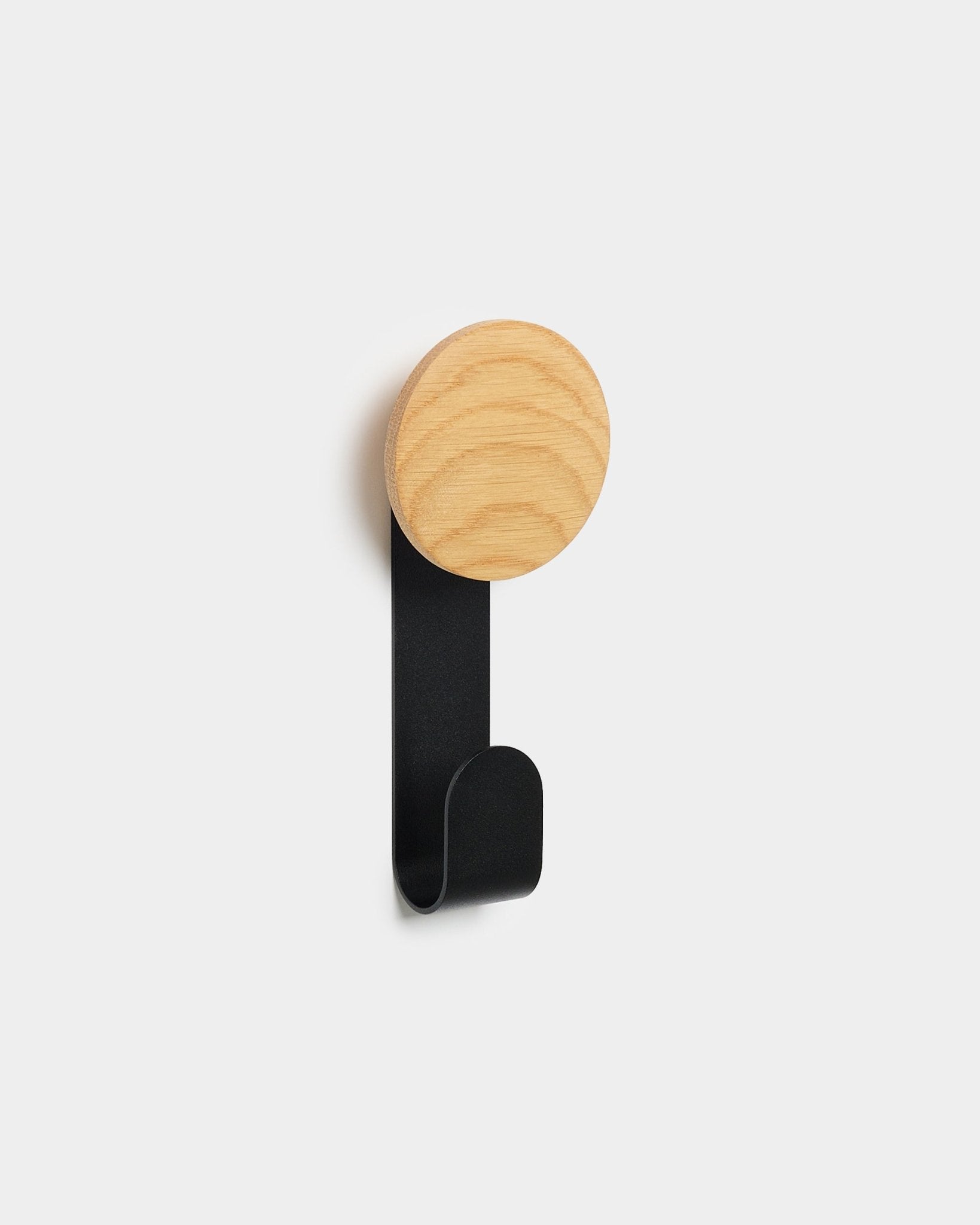 L’appendiabiti Linn Vertical di WoodUpp, con top rotondo in natural oak e gancio in metallo black, è pensato per appendere accessori ai pannelli acustici in legno Akupanels Nordic.