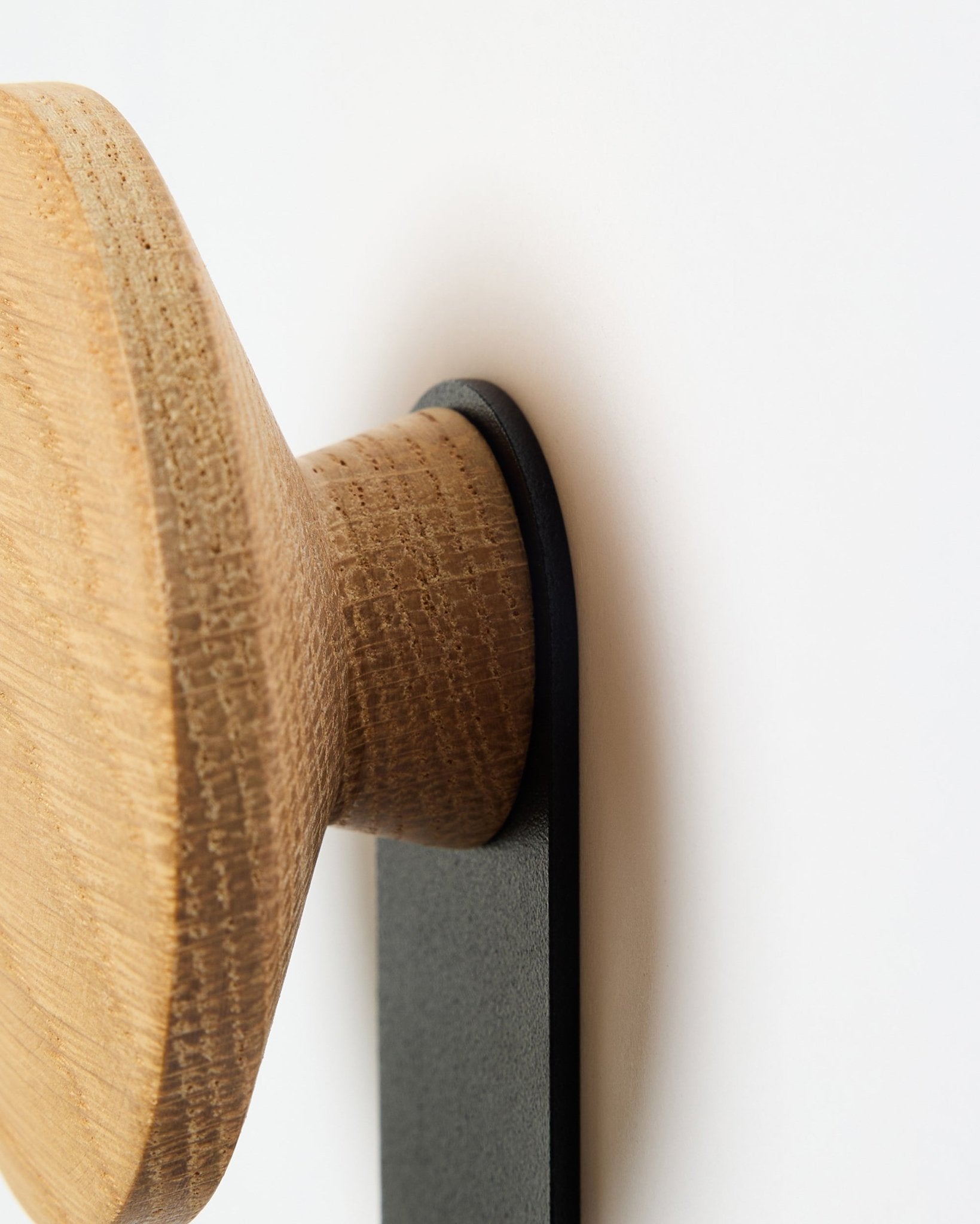 Primo piano dell’appendiabiti Linn Vertical in natural oak di WoodUpp, un accessorio con pomello rotondo in legno montato su una staffa black, progettato per pannelli acustici Akupanel.