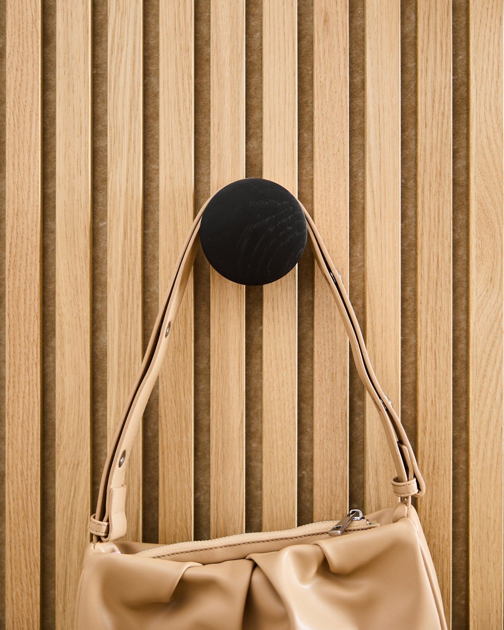 Borsa Beige appesa a un/una Linn | Single Hanger WoodUpp in Black Oak, montato/a su un pannello acustico a doghe Akupanel in legno chiaro.