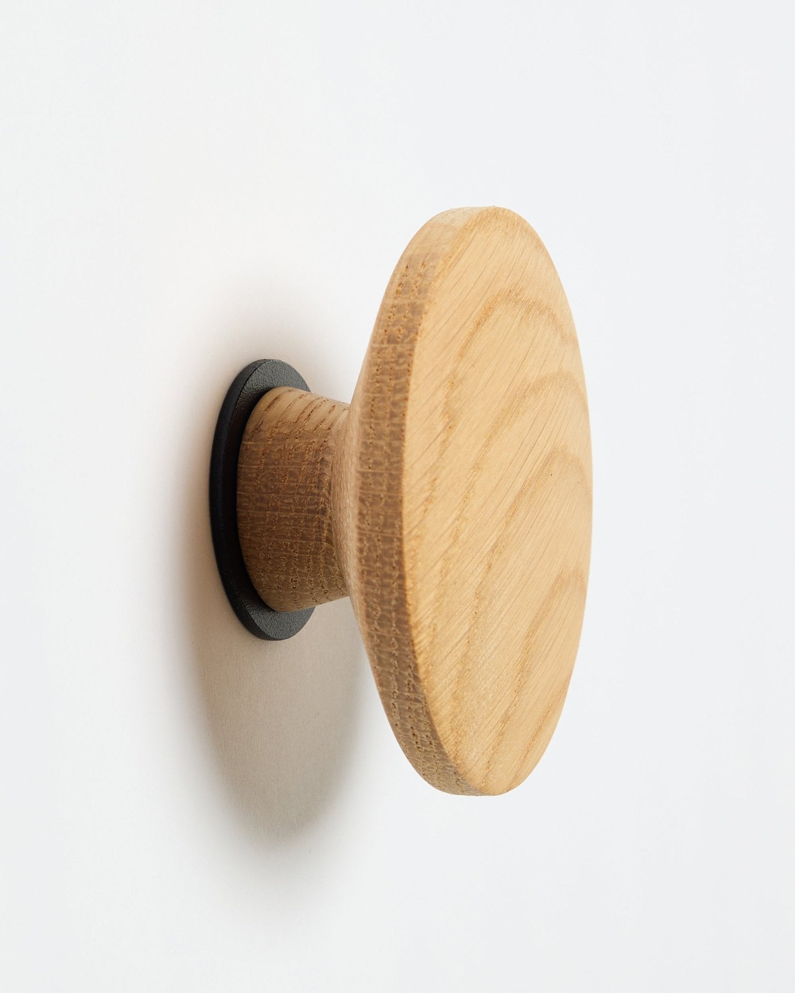 WoodUpp Linn I Single Hanger in natural oak, un gancio da parete rotondo con base black, progettato come accessorio da montare sui pannelli acustici in legno Akupanel.