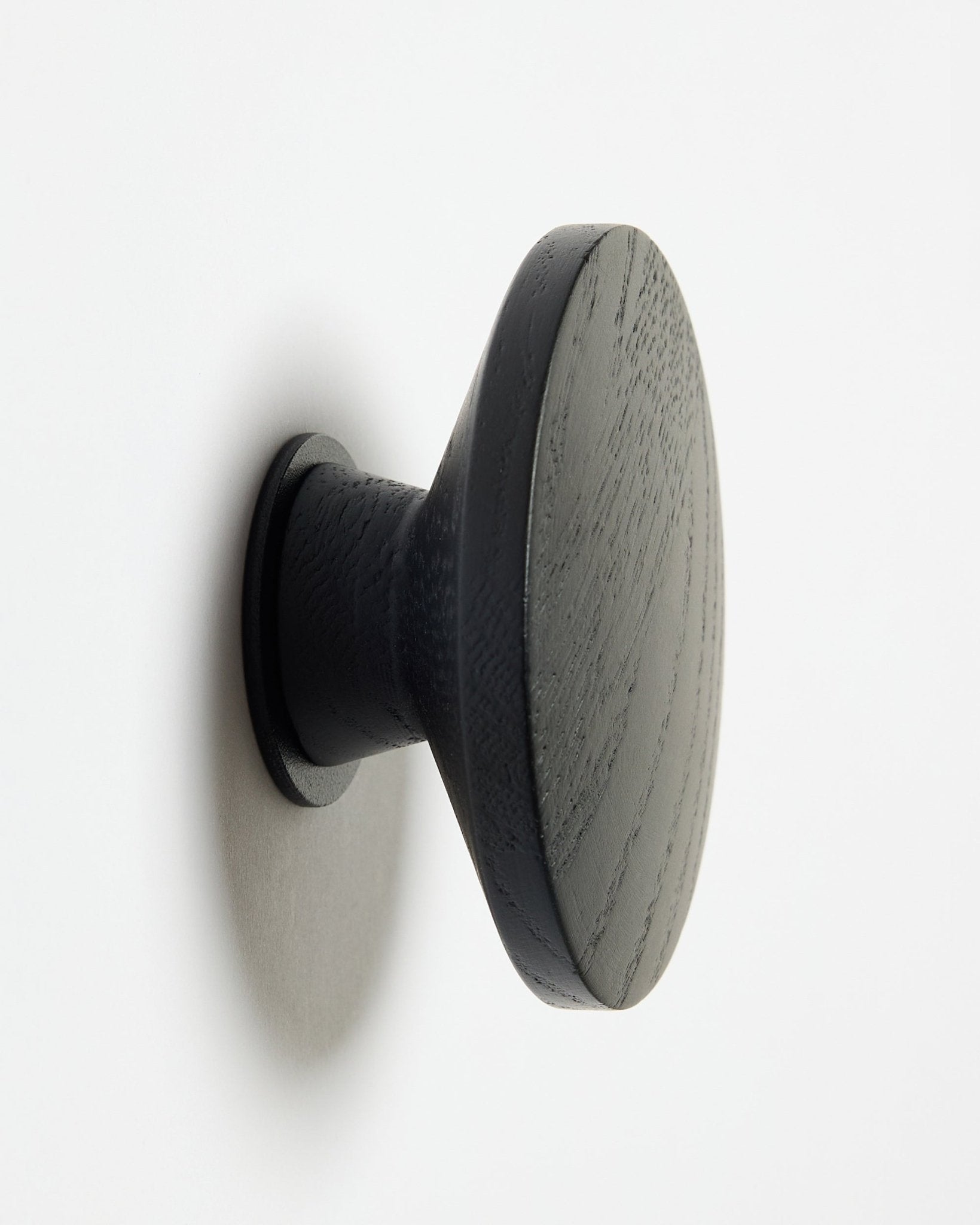 Un/Una Linn | Single Hanger rotondo/a black oak di WoodUpp, progettato/a come accessorio per pannelli acustici in legno Akupanel, montato/a su una superficie bianca con una lieve ombra sul lato sinistro.