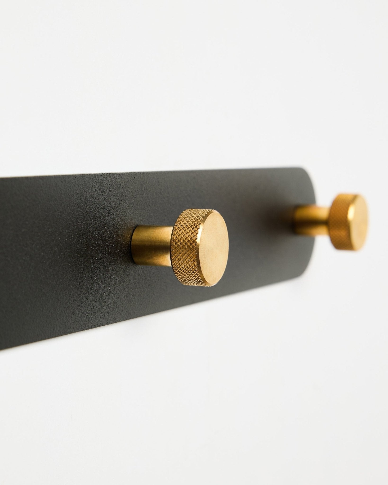 Coat Hook Rack WoodUpp Norr, modello X7, con due ganci cilindrici black e brass su un supporto black, mostrato su sfondo bianco.