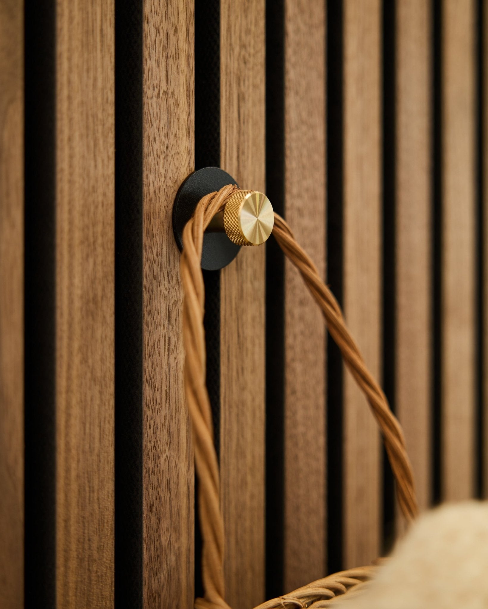Gancio appendiabiti WoodUpp Norr in black e brass, montato su una base Akupanel in legno Pannello acustico, sostiene un manico intrecciato color cuoio.