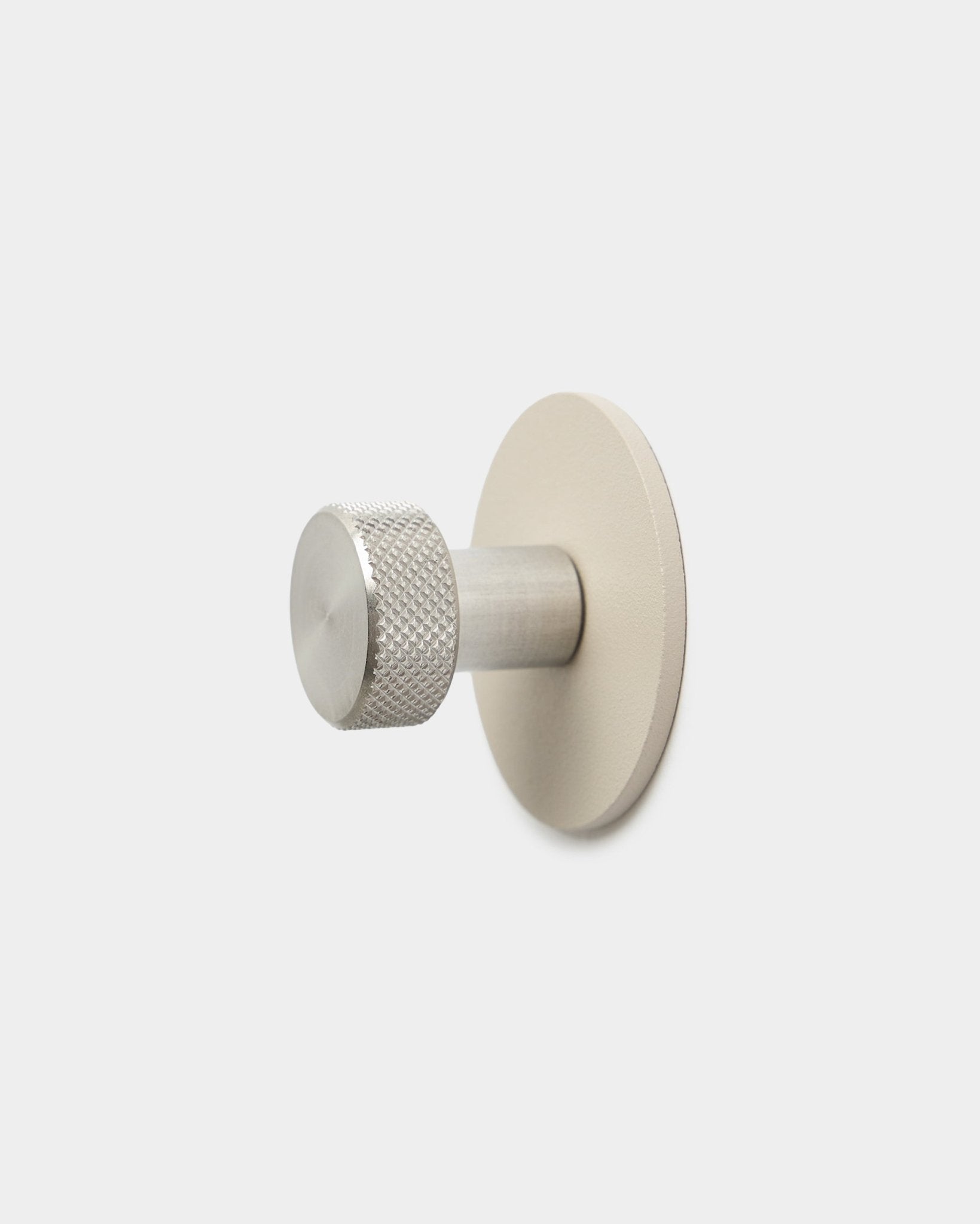 Gancio appendiabiti WoodUpp Norr in beige e acciaio inox steel, con estremità cilindrica texturizzata e base rotonda, accessorio per Akupanel, su sfondo bianco semplice.