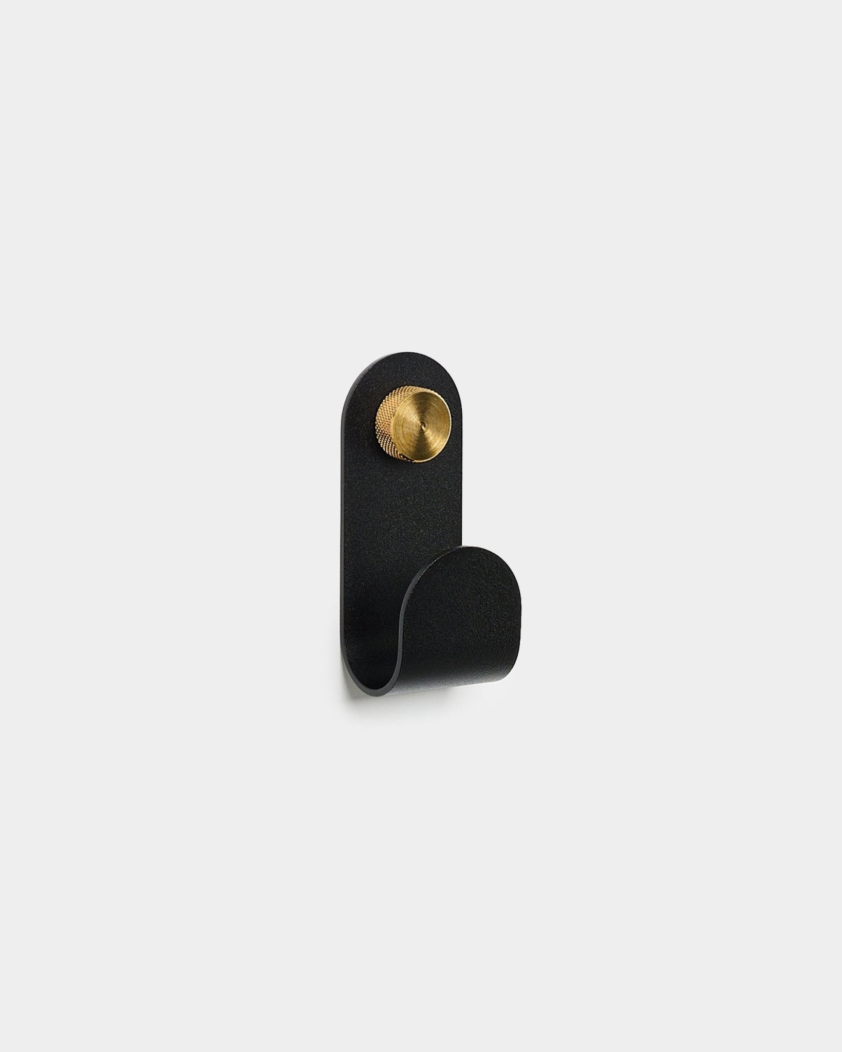 Il Norr Single Hanger in black di WoodUpp, con un design curvo e un dettaglio rotondo in brass, è mostrato su uno sfondo bianco semplice.