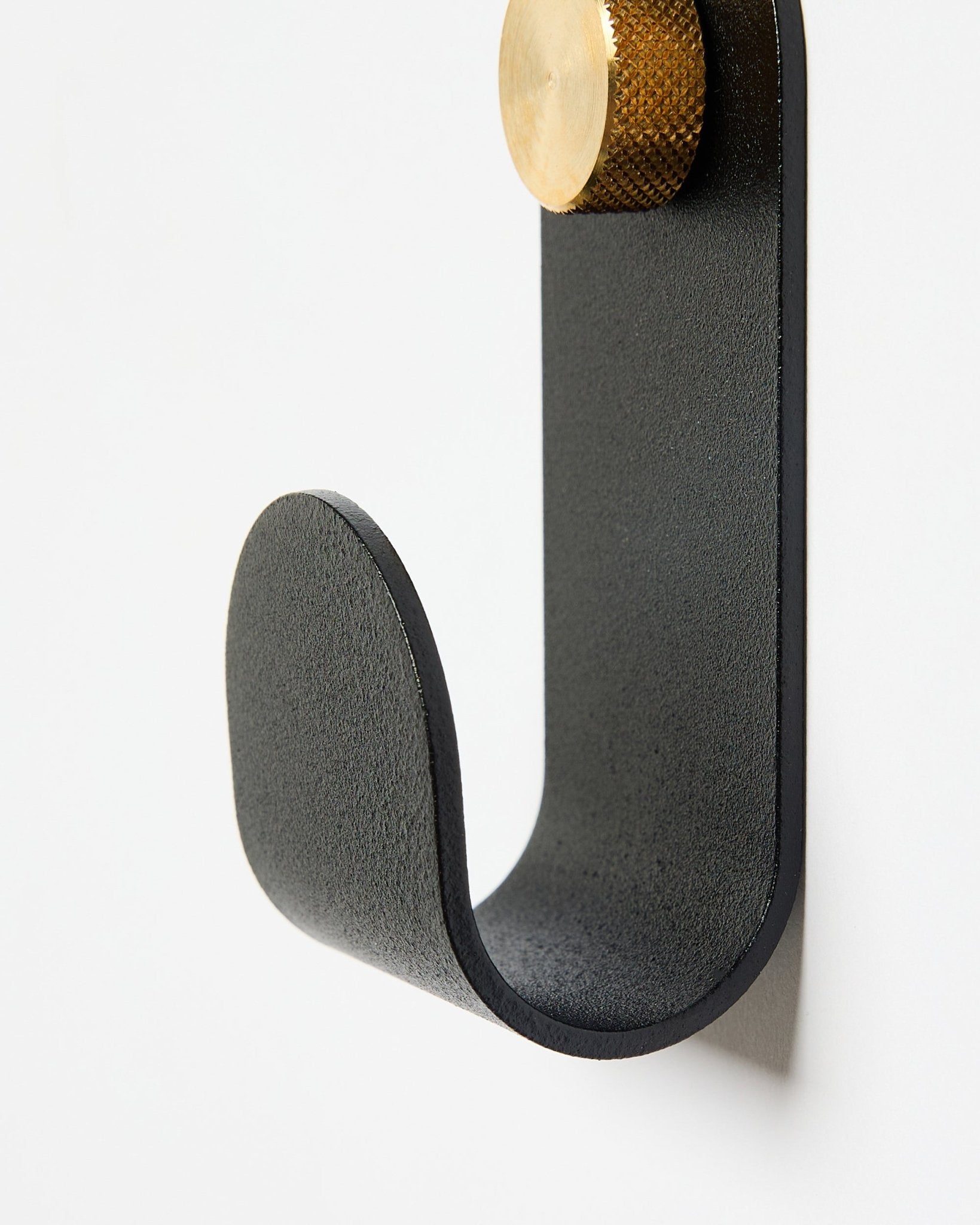 Il Norr Single Hanger di WoodUpp ha un braccio curvo in metallo black con terminale dorato, pensato come accessorio da usare con i pannelli acustici su pareti bianche.