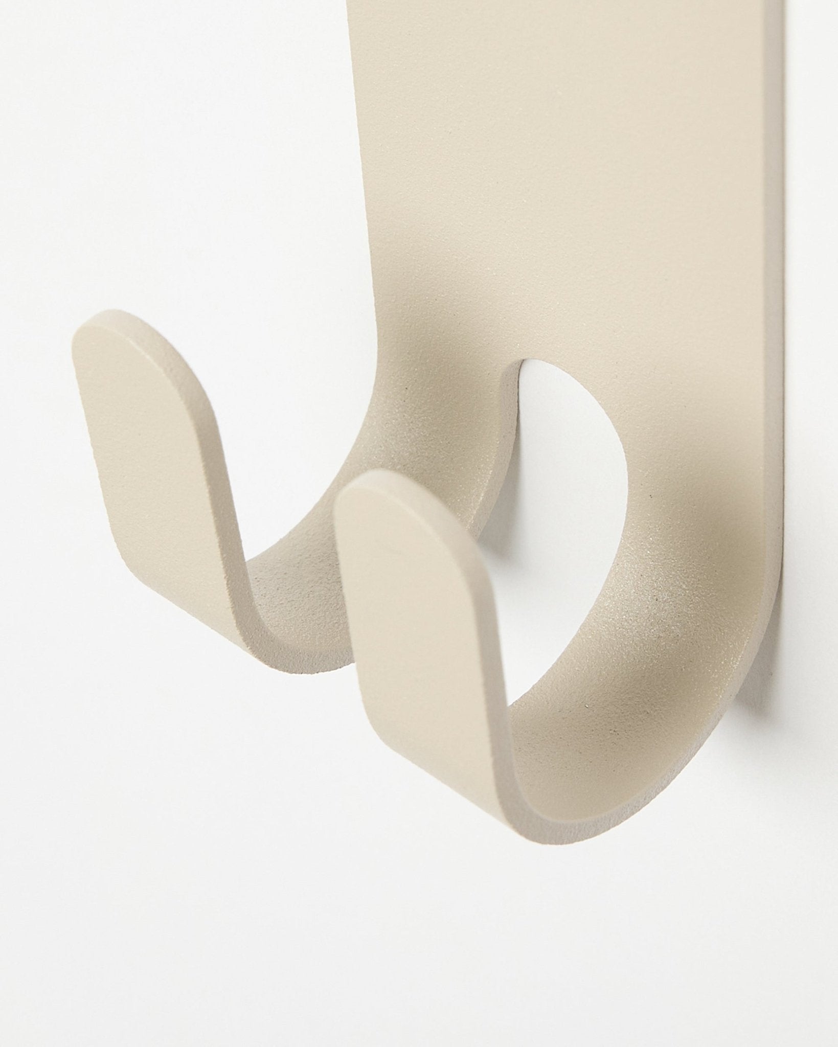 Primo piano del Norr Double Hanger in beige di WoodUpp, un gancio appendiabiti in metallo dal design minimalista installato su una slatwall Pannello acustico in colored chiaro.
